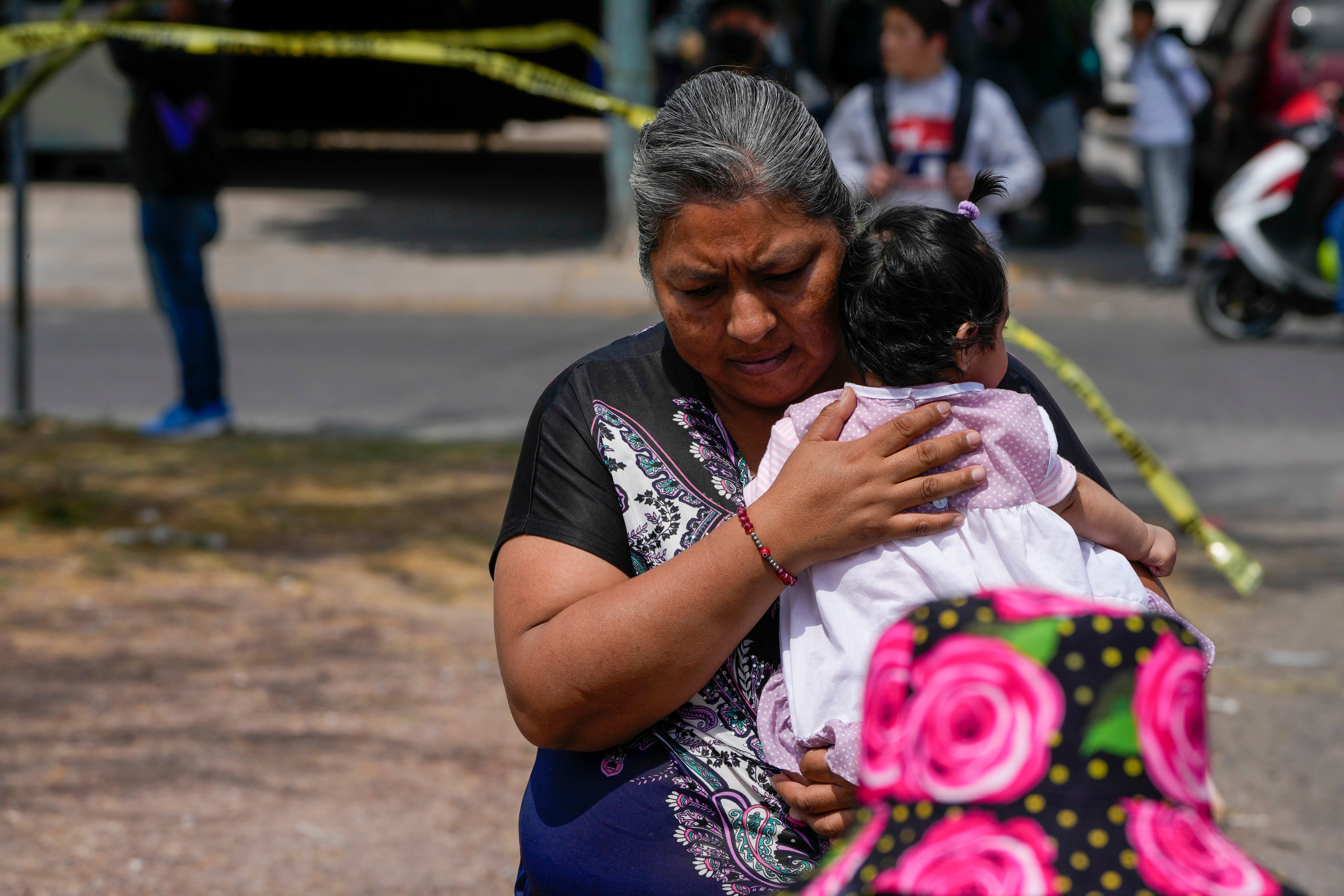 A resident cradles an infant as she walks past a crime scene where a passenger was shot dead inside a bus