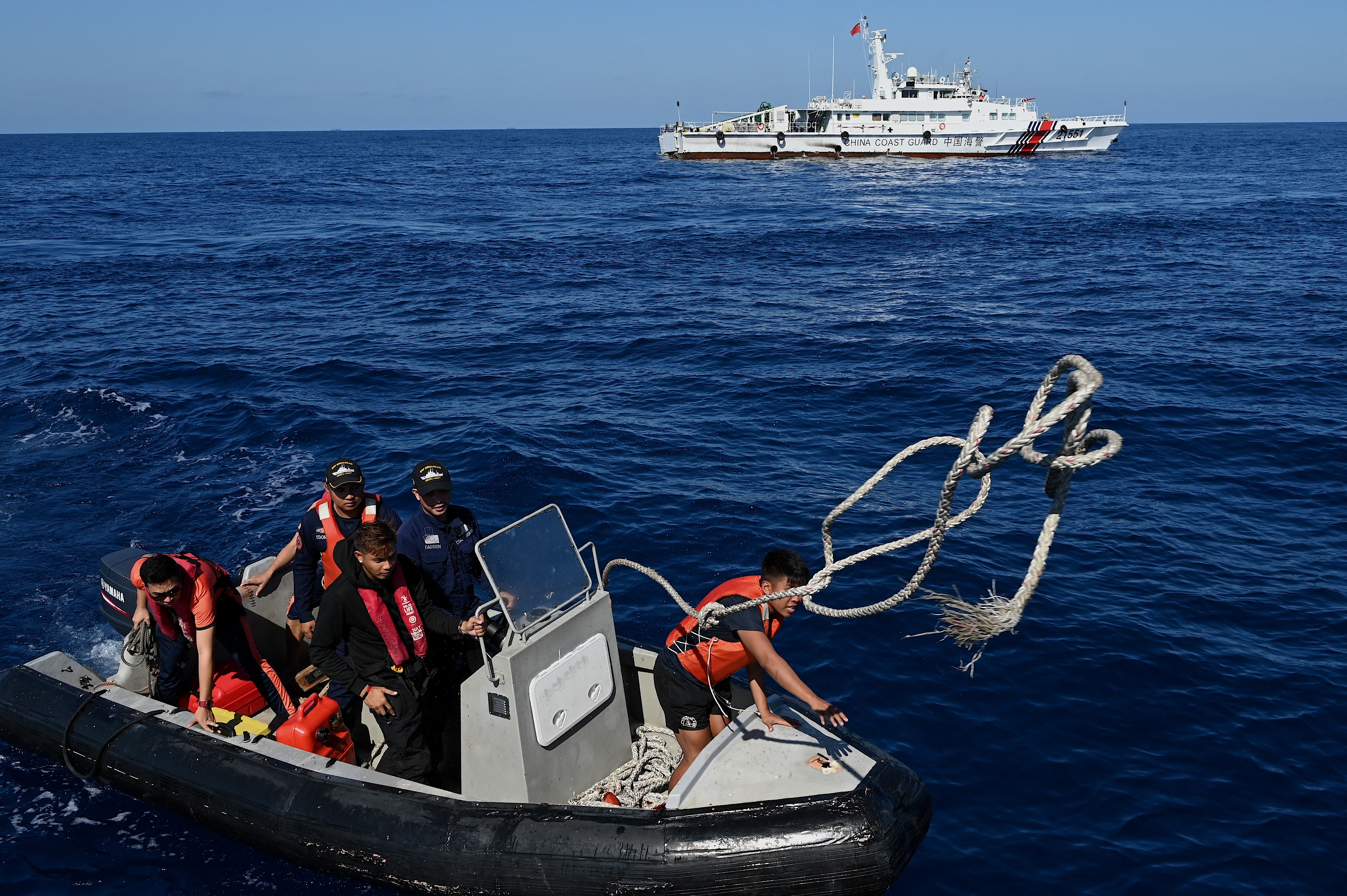 This photo taken on 5 March 2024 shows Philippine Coast Guard personnel onboard a rubber boat after they delivered medical supplies to the military chartered Unaizah 4 May as a China Coast Guard vessel (back) sails nearby during a supply mission to Second Thomas Shoal in the disputed South China Sea