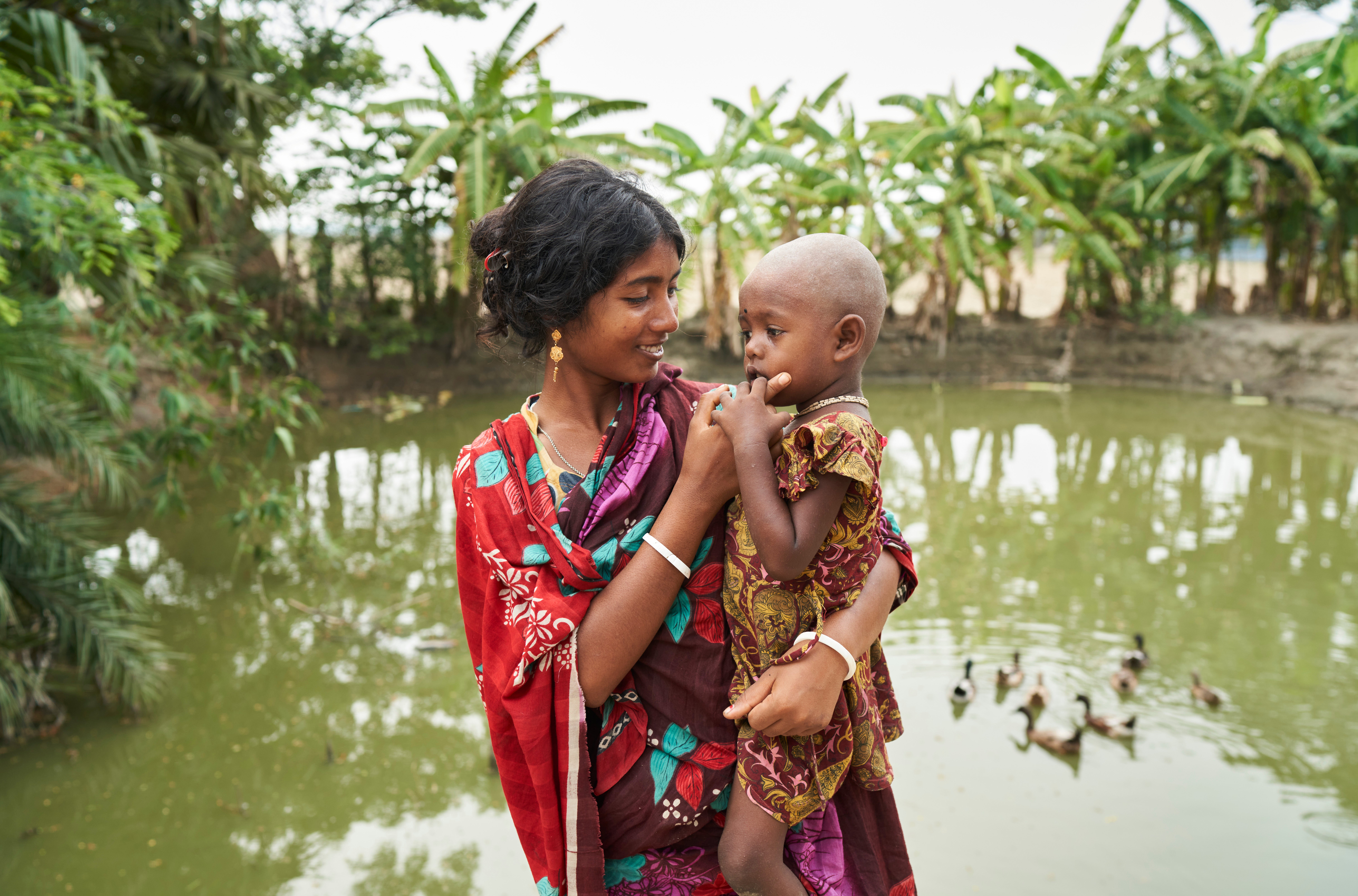 Jhorna, 22, and her daughter Obonita, 3, in front of the pond they use for washing