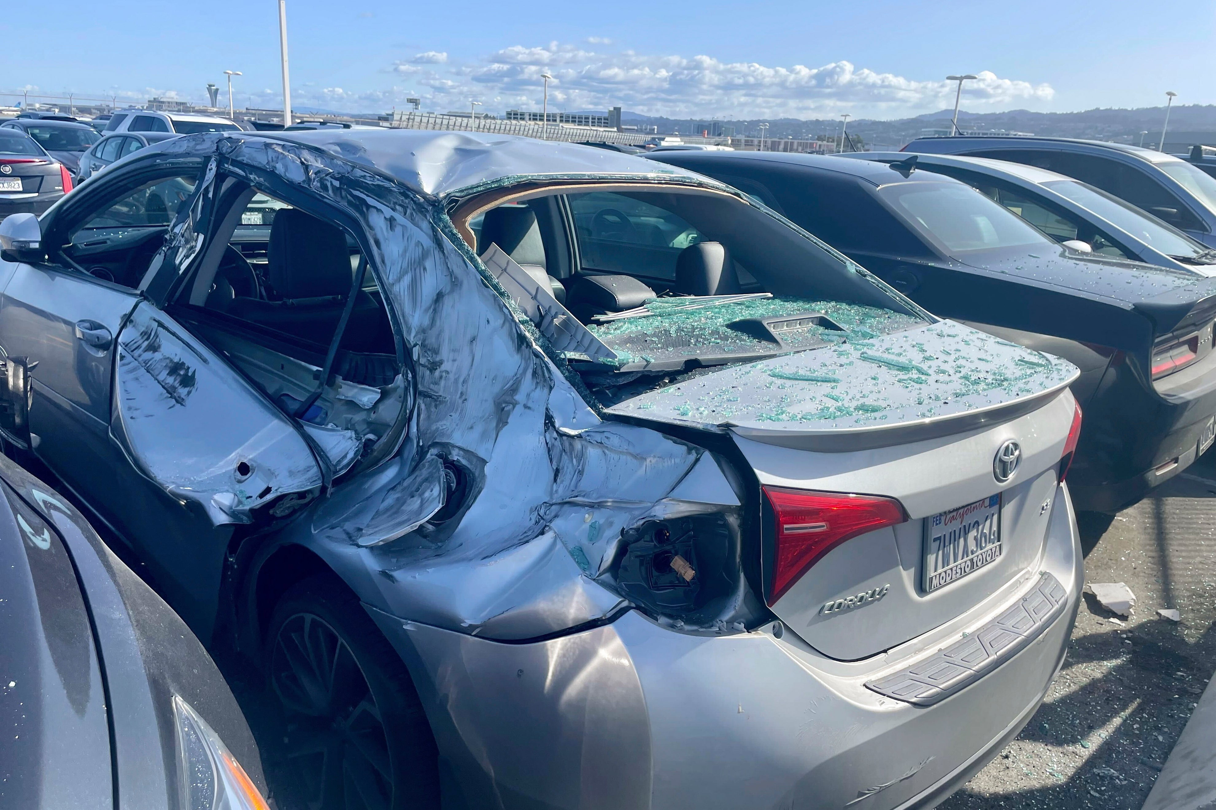 A damaged car is seen in an on-airport employee parking lot after tire debris from a Boeing 777 landed on it at San Francisco International Airport