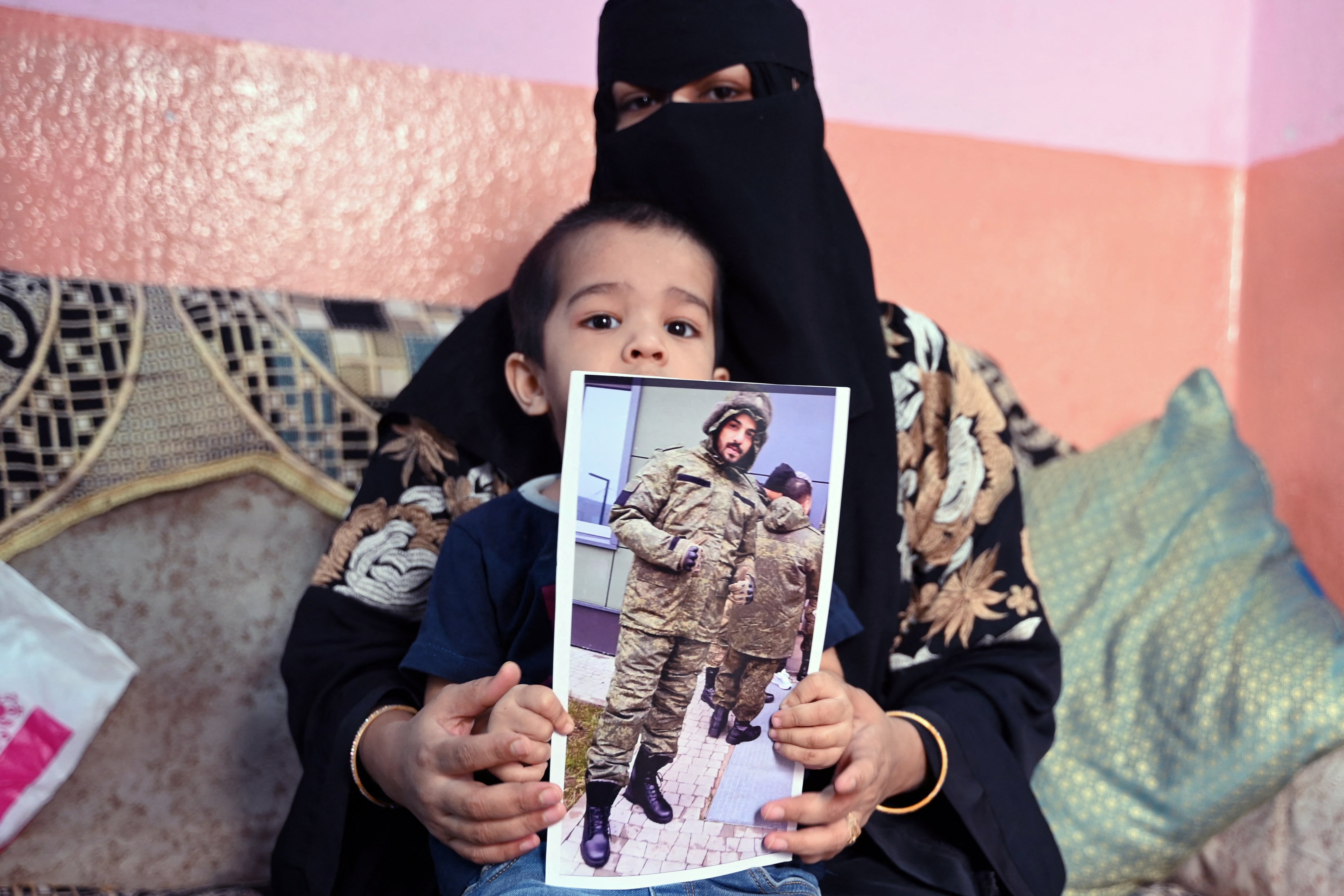 This photo taken on 22 February 2024 shows a picture printout of Indian national Mohammed Asfan, seen wearing Russian military fatigues who last called family from the southern Russian city of Rostov-on-Don before being deployed amid the conflict in Ukraine, being held by his wife Asma Shireen and their child in Hyderabad