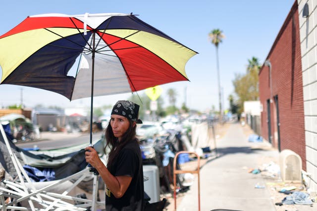 <p> Roni stands beneath an umbrella in a section of the The Zone' Phoenix, Arizona's largest homeless encampment, amid the city's worst heat wave on record on 25 July 2023</p>