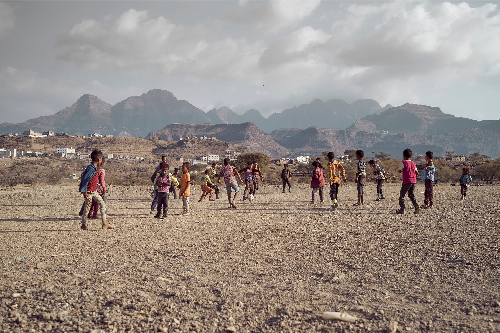 Children play football against the backdrop of the mountains in an IDP camp in Turbah town