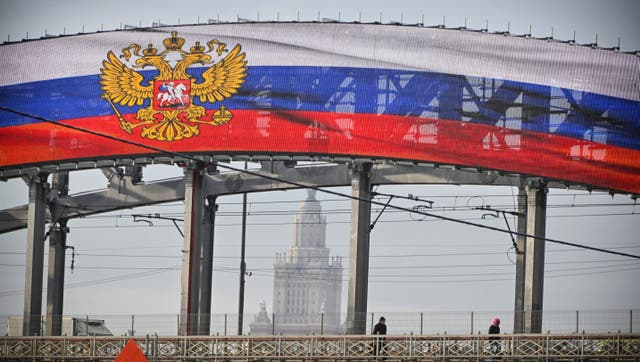 <p>A mediascreen set up on a railway bridge displays the Russian State Emblem and the national tricolor flag in western Moscow on February 14, 2024, in front of the main building of the Moscow State University</p>