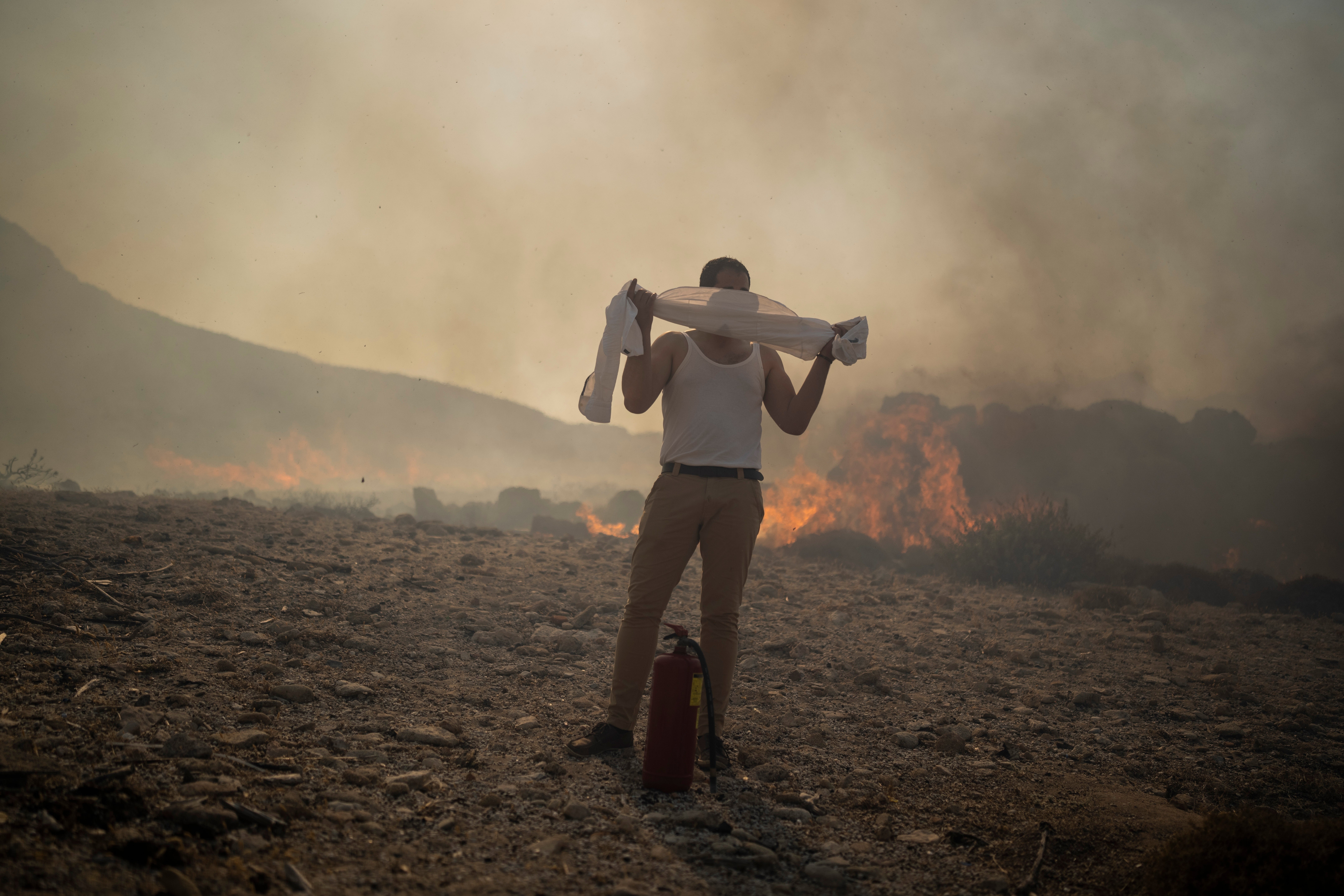 FILE - A man wraps his shirt over his face as he tries to extinguish a fire, near the seaside resort of Lindos, on the Aegean Sea island of Rhodes, southeastern Greece, on July 24, 2023