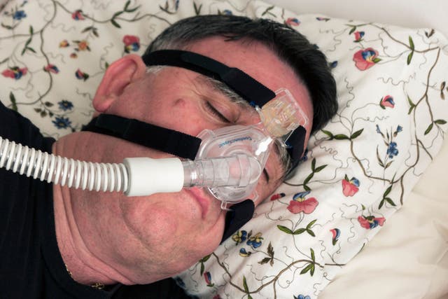 <p>A man using a CPAP face mask and machine used for the treatment of sleep apneoa</p>