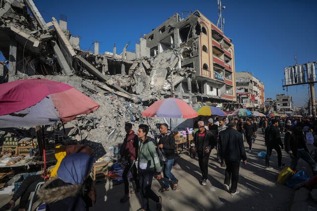 <p>Palestinians walk past kiosks set up next to destroyed buildings along a street on the first day of Ramadan in Al Nusairat refugee camp in Gaza on 11 March. </p>