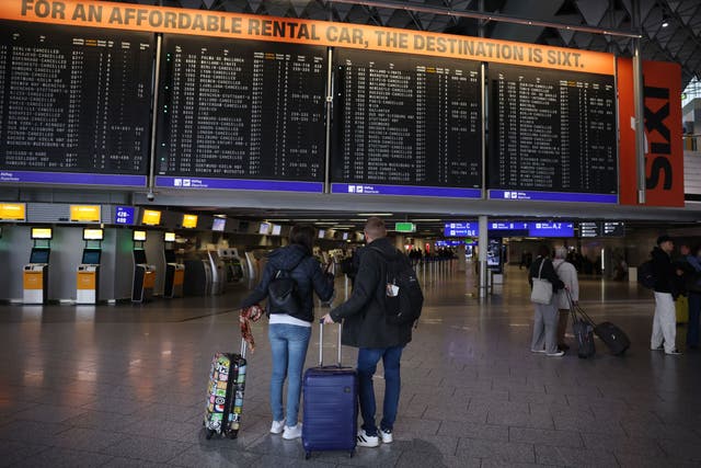 <p>Passengers stand in front of a departures board at Frankfurt Airport on Tuesday 12 March</p>