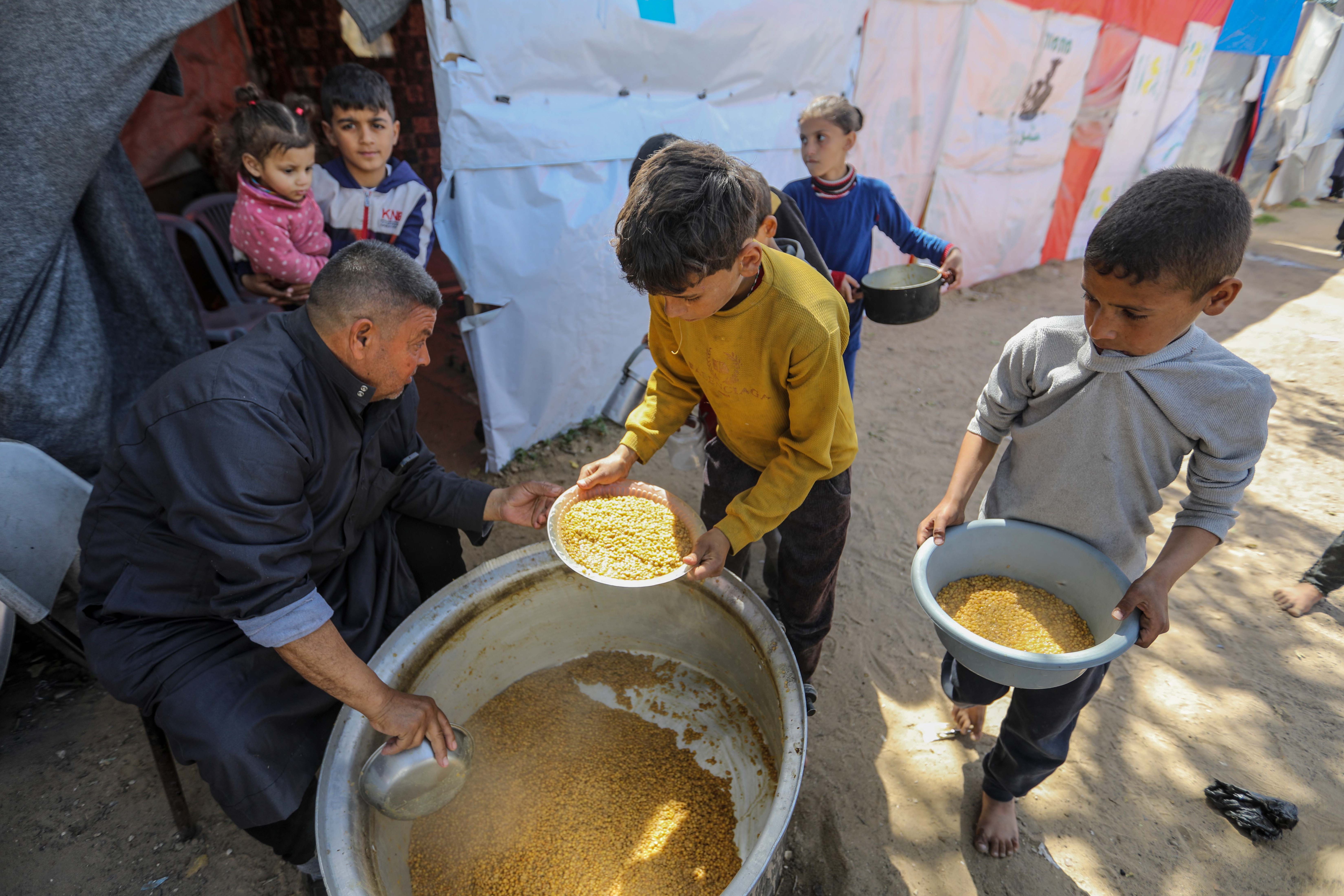 Citizens queue for food that is cooked in large pots and distributed for free in Rafah, southern Gaza