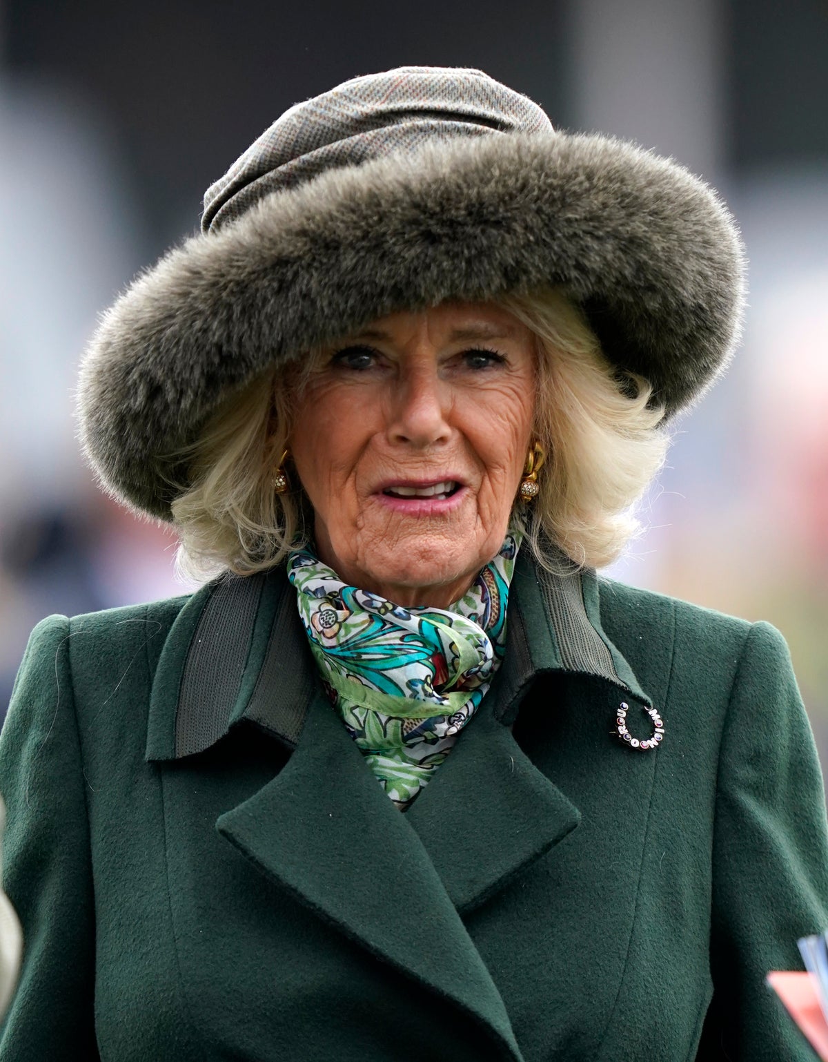 Queen Camilla holds onto her hat as she arrives at Cheltenham without Charles