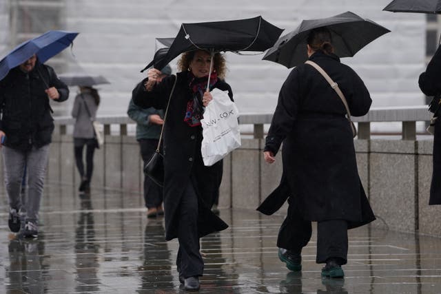 <p>People walk in the rain over London Bridge in central London</p>