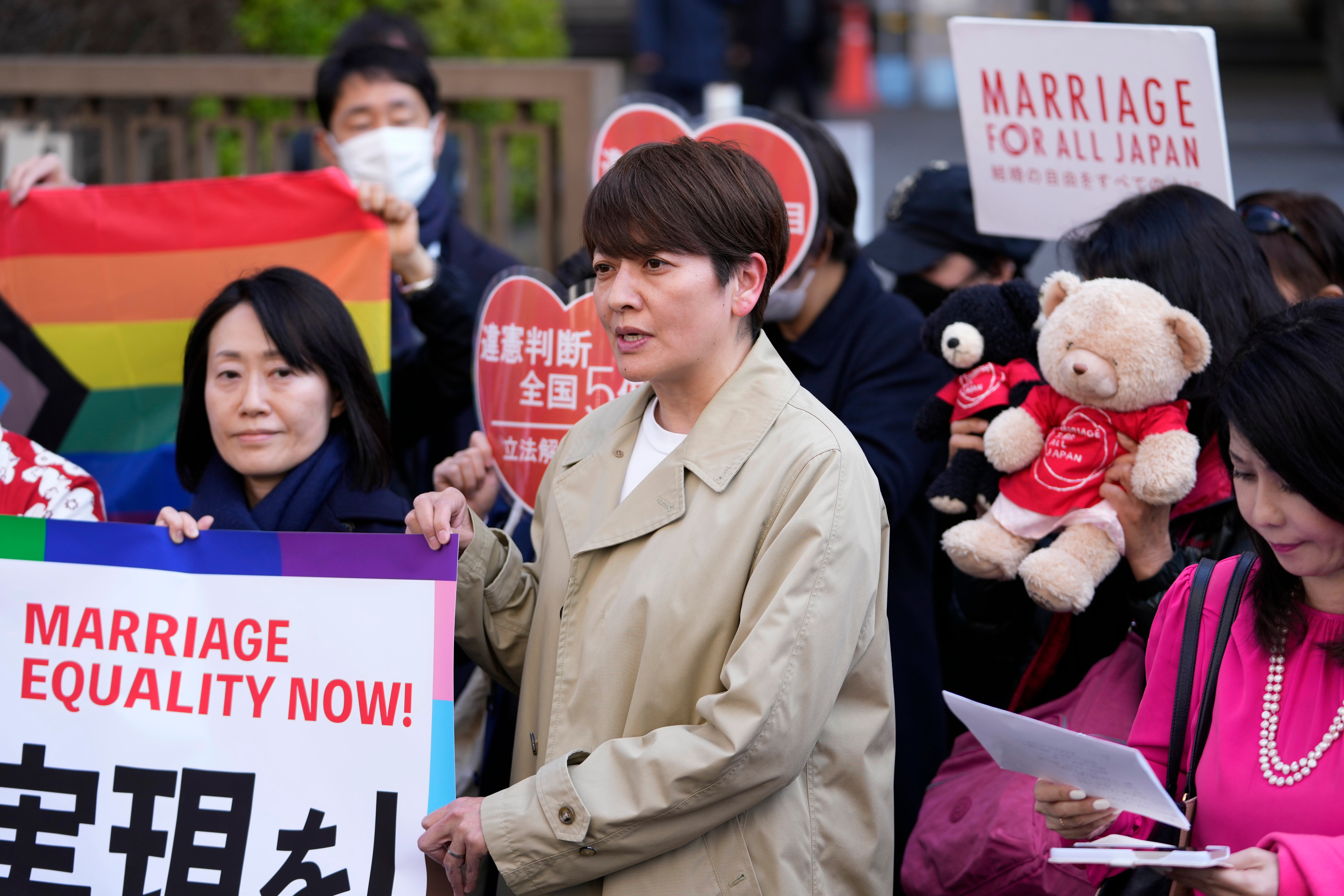 One of the plaintiffs, in a beige coat, center, speaks in front of media members by the main entrance of the Tokyo district court