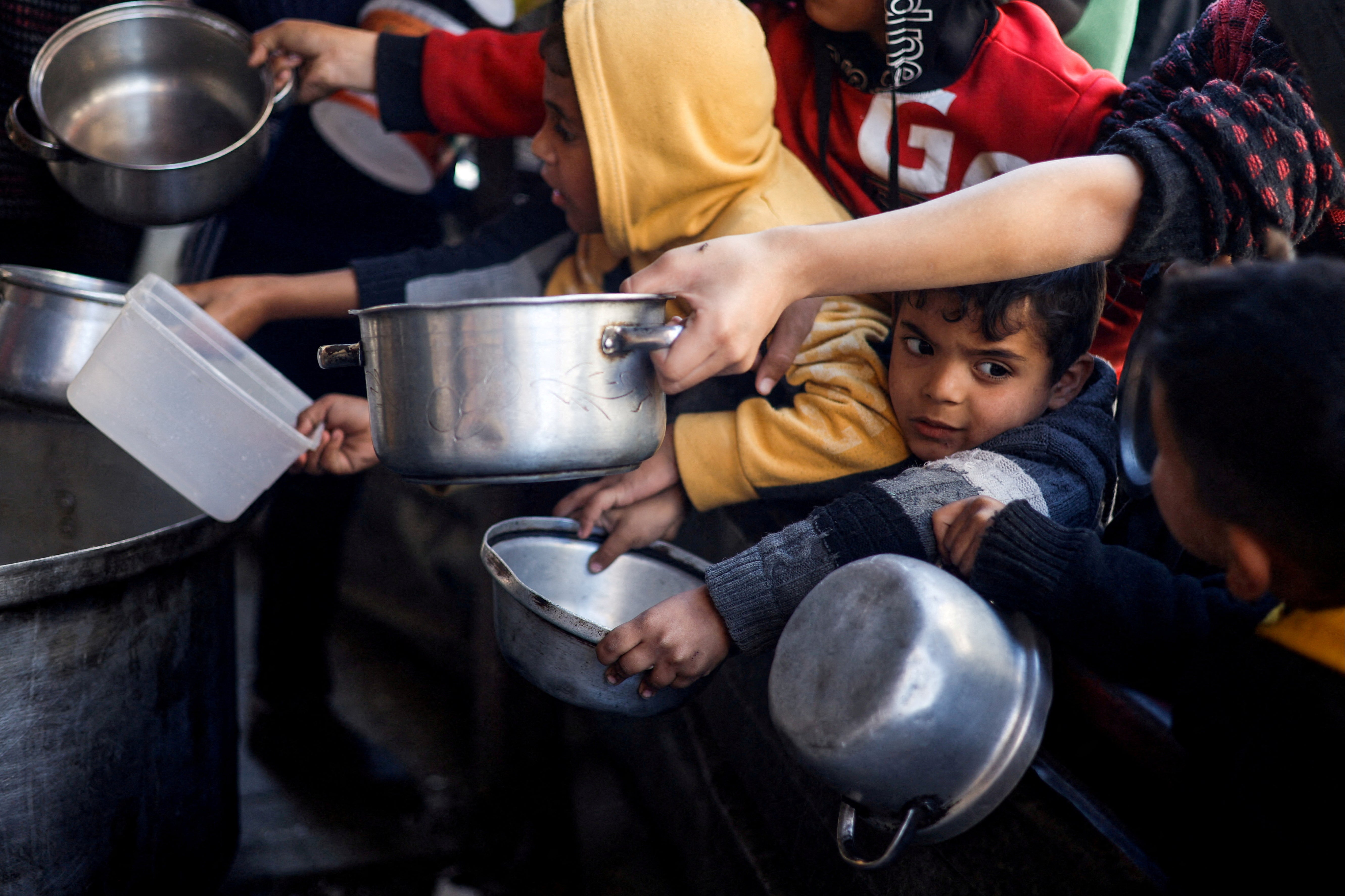 Palestinian children wait to receive food cooked by a charity kitchen amid shortages of supplies in Rafah