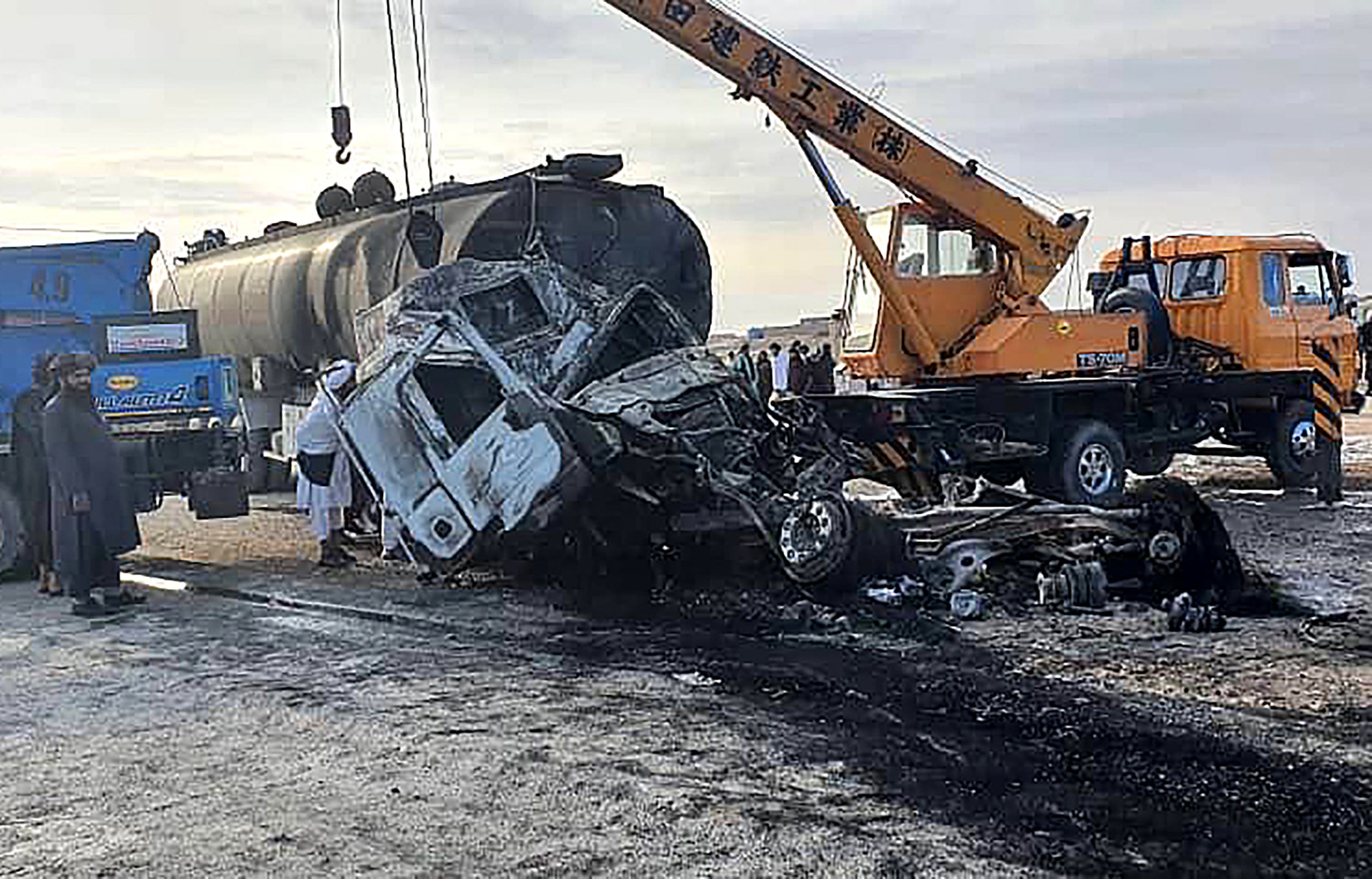 Security personnel and volunteers standing near the wreckage of burned passenger bus and oil tanker on the Herat-Kandahar highway in Grishk district of Helmand province