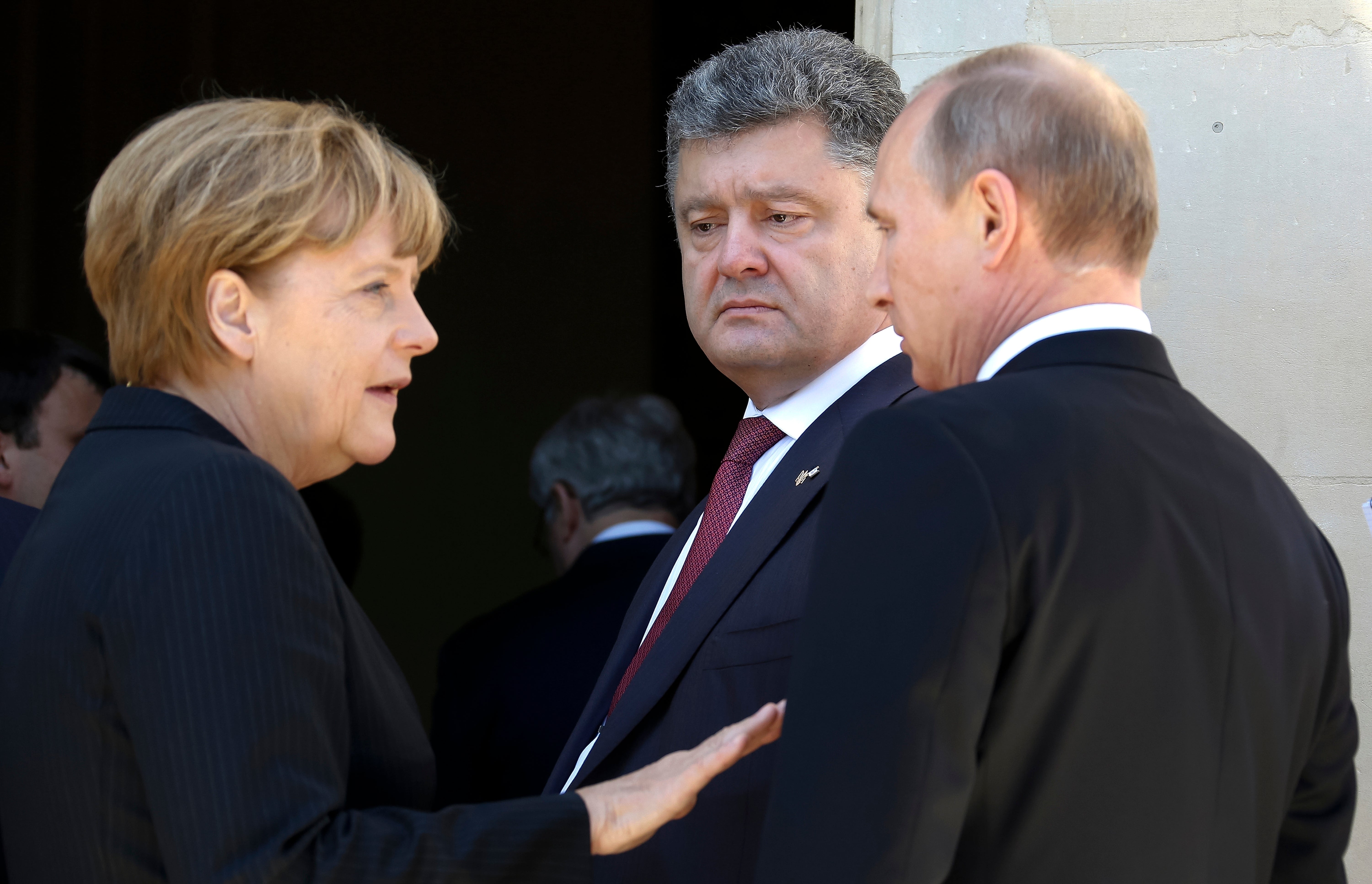 German Chancellor Angela Merkel, left, Russian President Vladimir Putin, right, and then Ukrainian president-elect Petro Poroshenko, center, talk at the 70th anniversary of D-Day in Benouville in Normandy, France, June 6, 2014