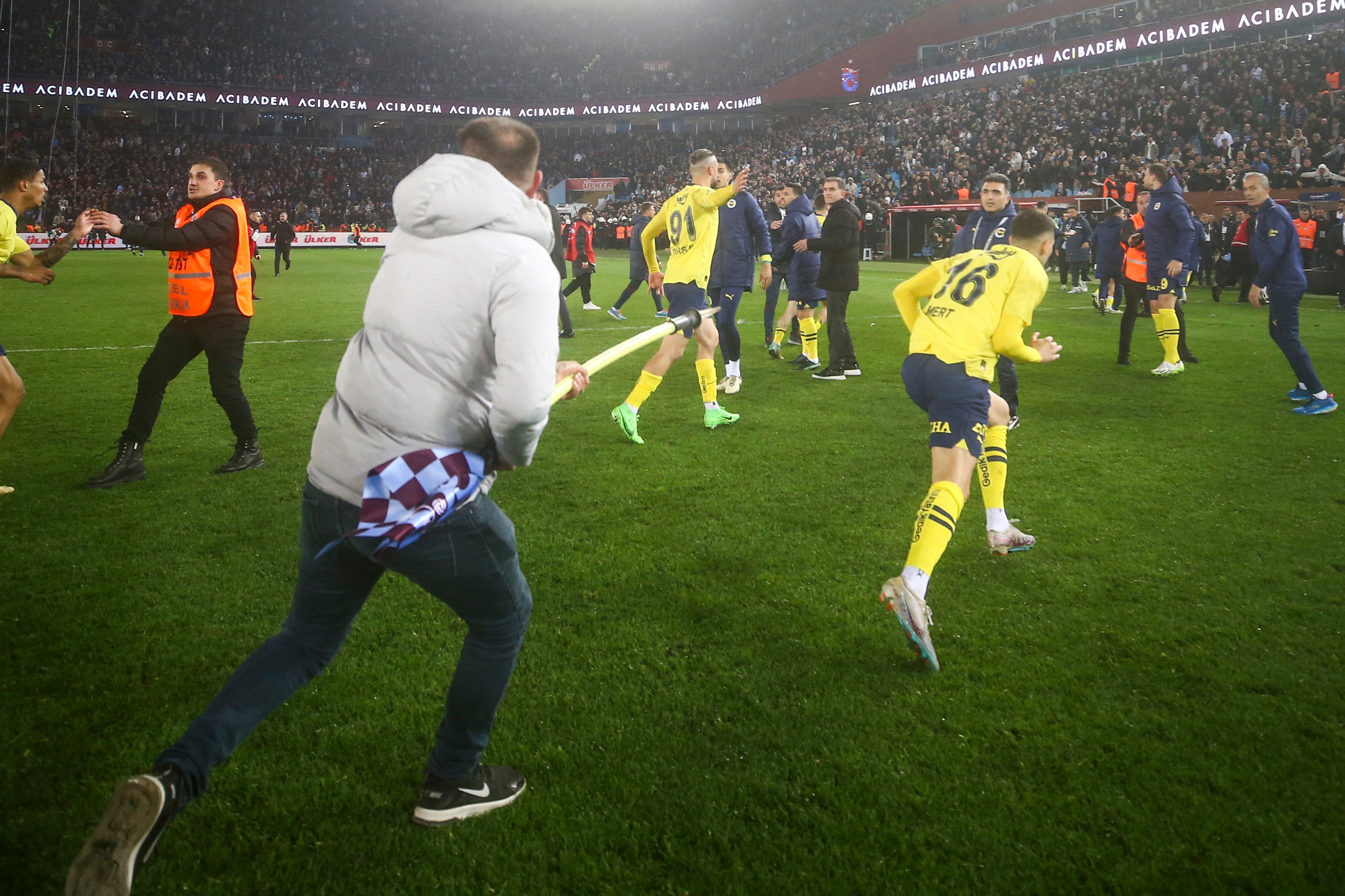 A Trabzonspor fan runs with a corner flag towards Fenerbahce's Mert Muldur