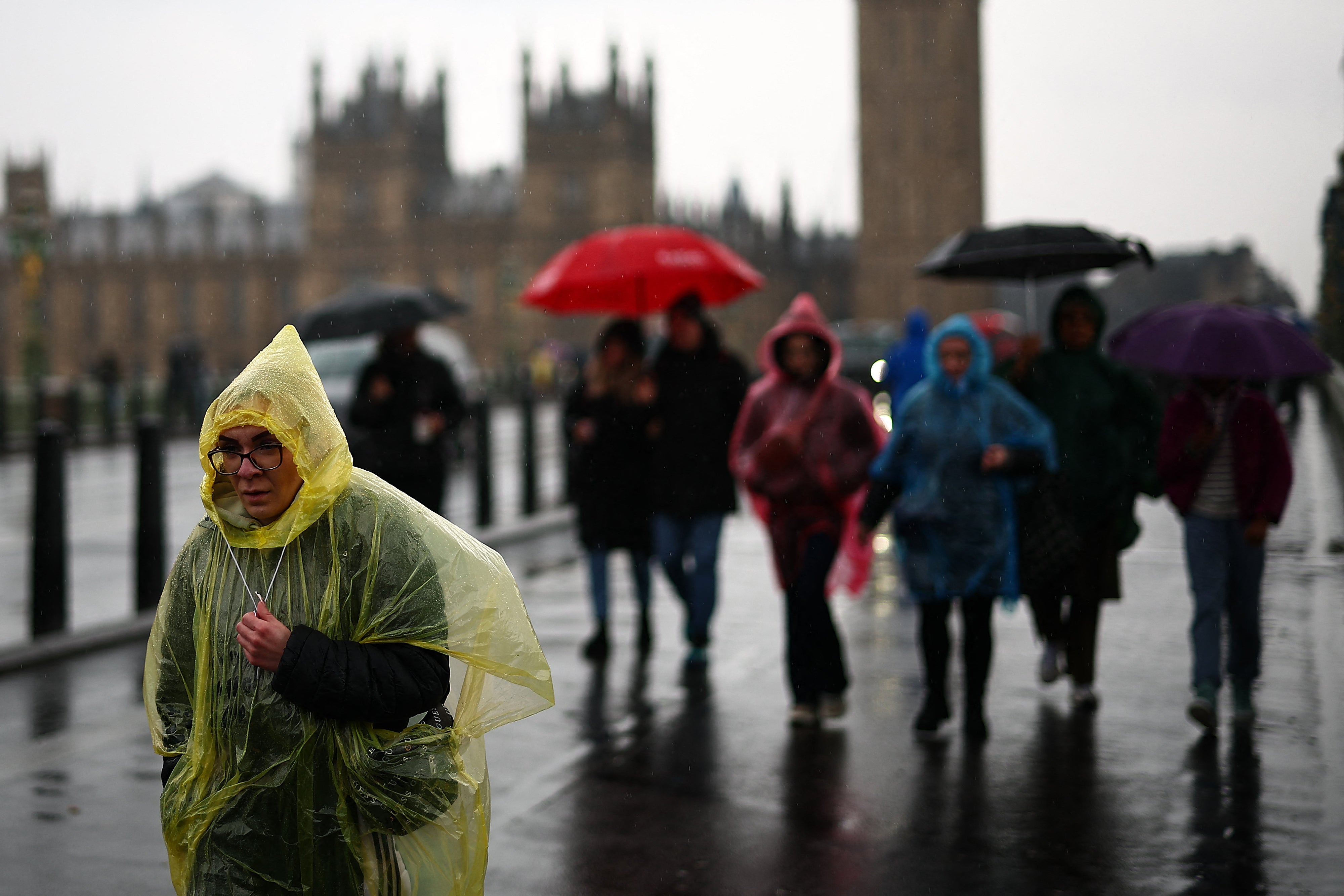 Tourists shelter from the rain as they walk over Westminster Bridge, with the Houses of Parliament in the background, in London on March 10, 2024. (Photo by HENRY NICHOLLS / AFP) (Photo by HENRY NICHOLLS/AFP via Getty Images)