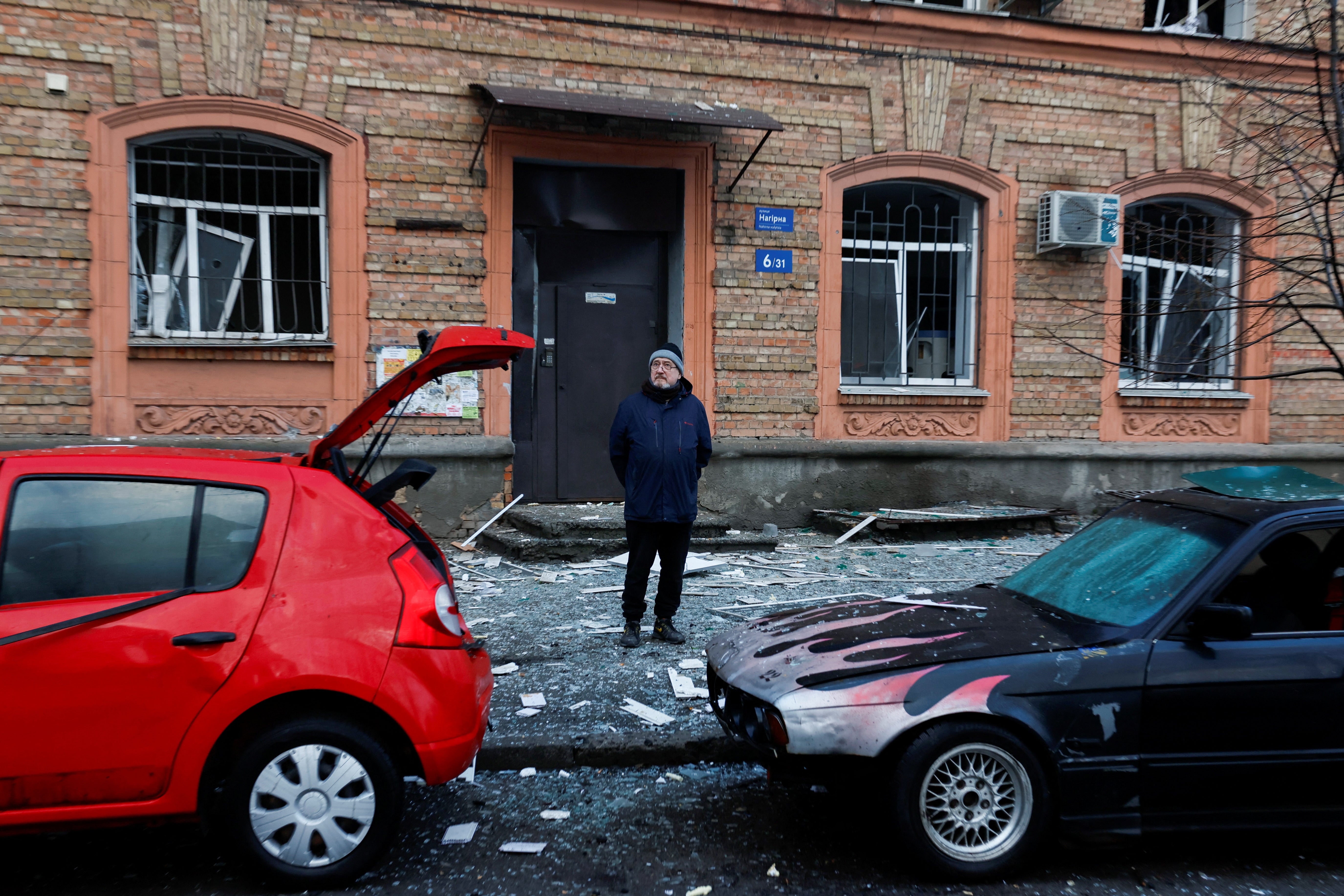 <p>A person stands behind destroyed vehicles at a site of a building, damaged during a Russian missile strike, amid Russia's attack on Ukraine, in Kyiv</p>