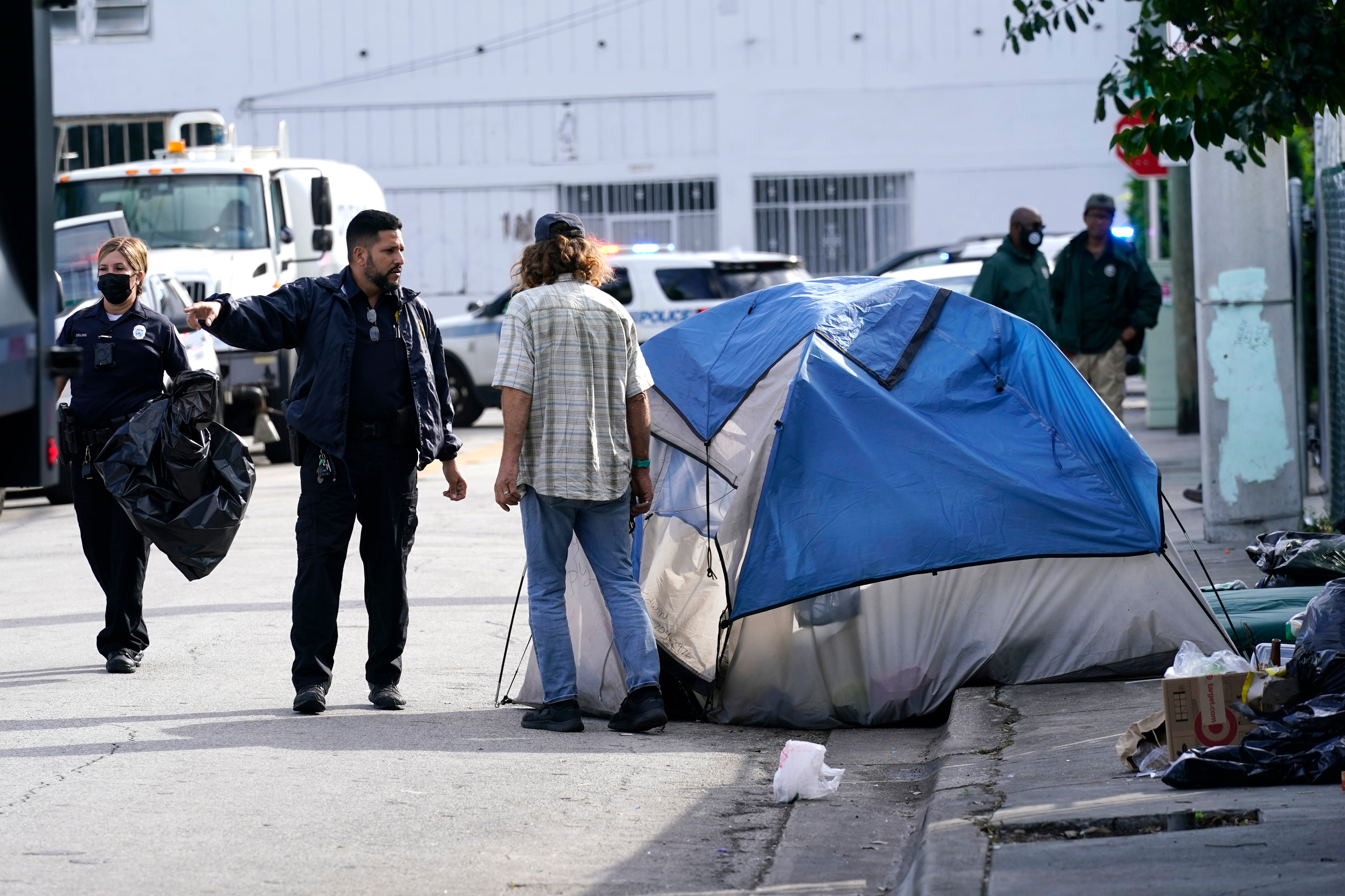 Miami police speak with an unhoused person before a street is cleared in 2021. Under a new Florida law, effective this October, unhoused people cannot sleep in public spaces.
