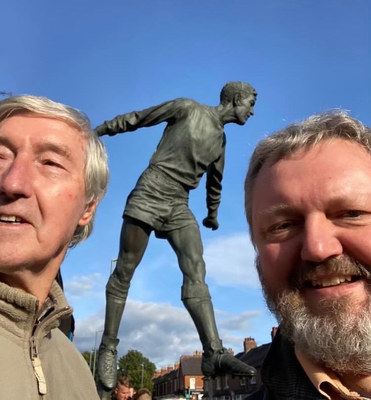 Hugh and Alan standing in front of the statue outside Carlisle United stadium, Brunton Park
