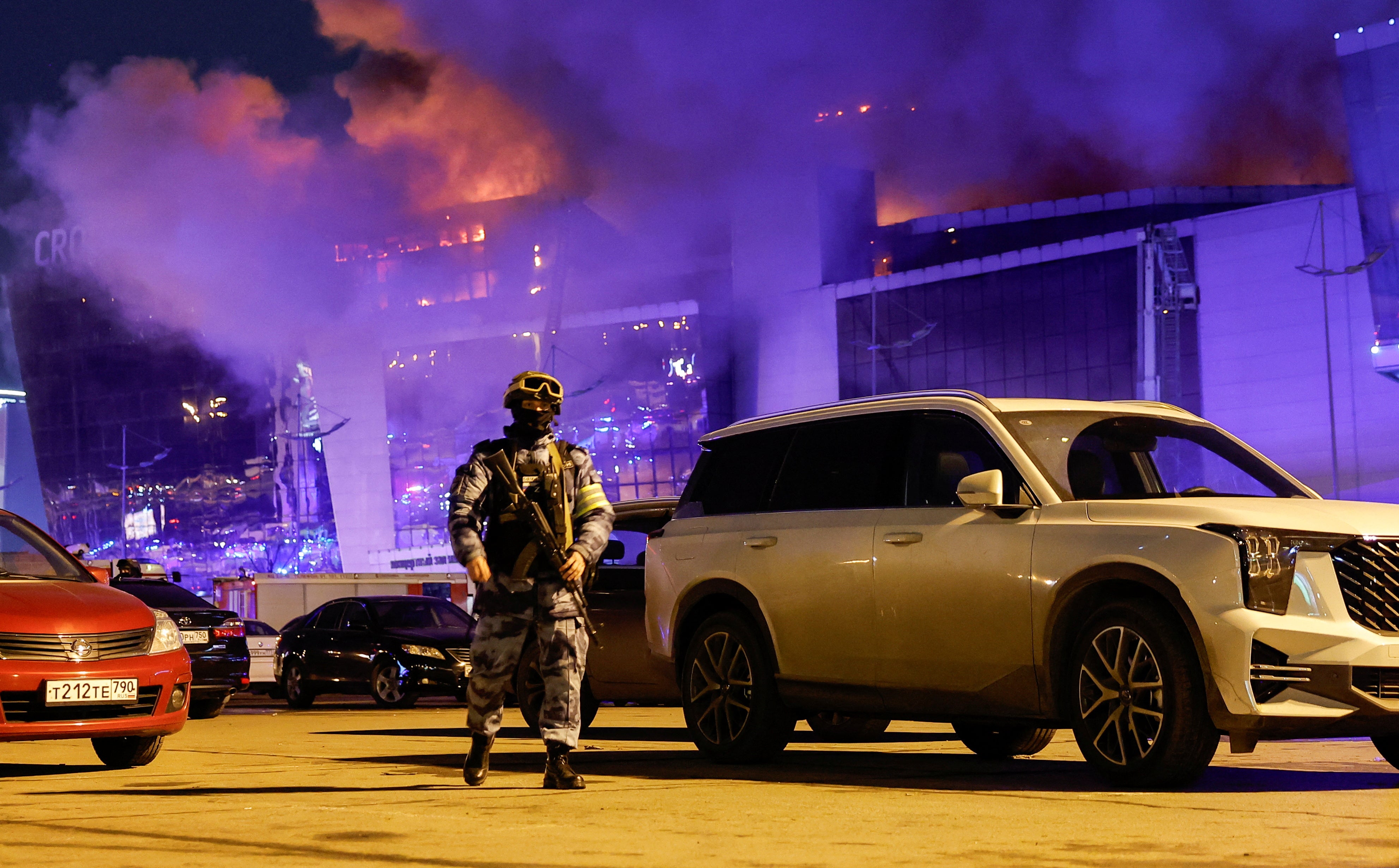 A Russian law enforcement officer walks at a parking area near the burning Crocus City Hall concert venue following a shooting incident, outside Moscow, Russia, 22 March 2024