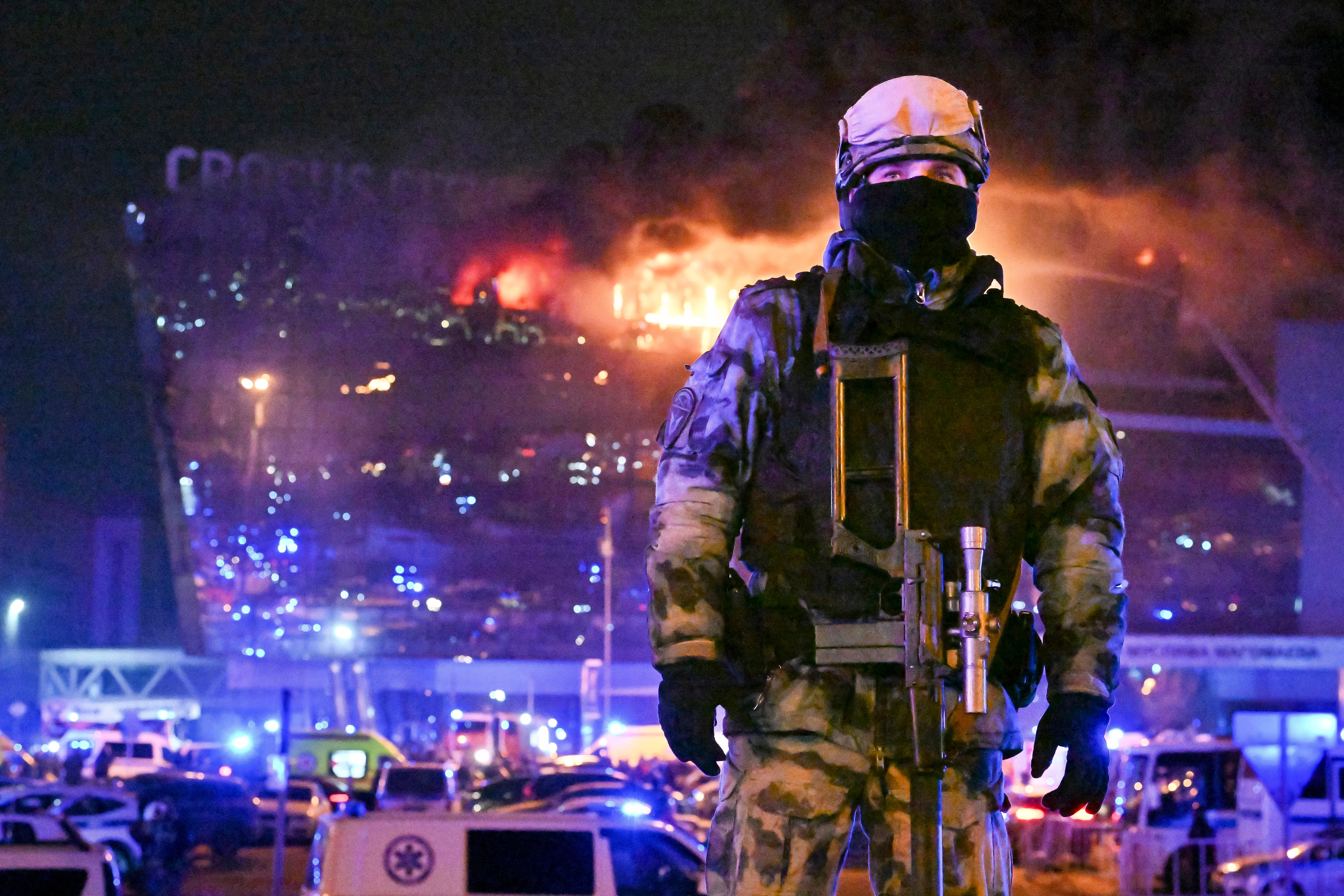 A Russian Rosguardia (national guard) serviceman secures an area as a massive blaze seen over Crocus City Hall