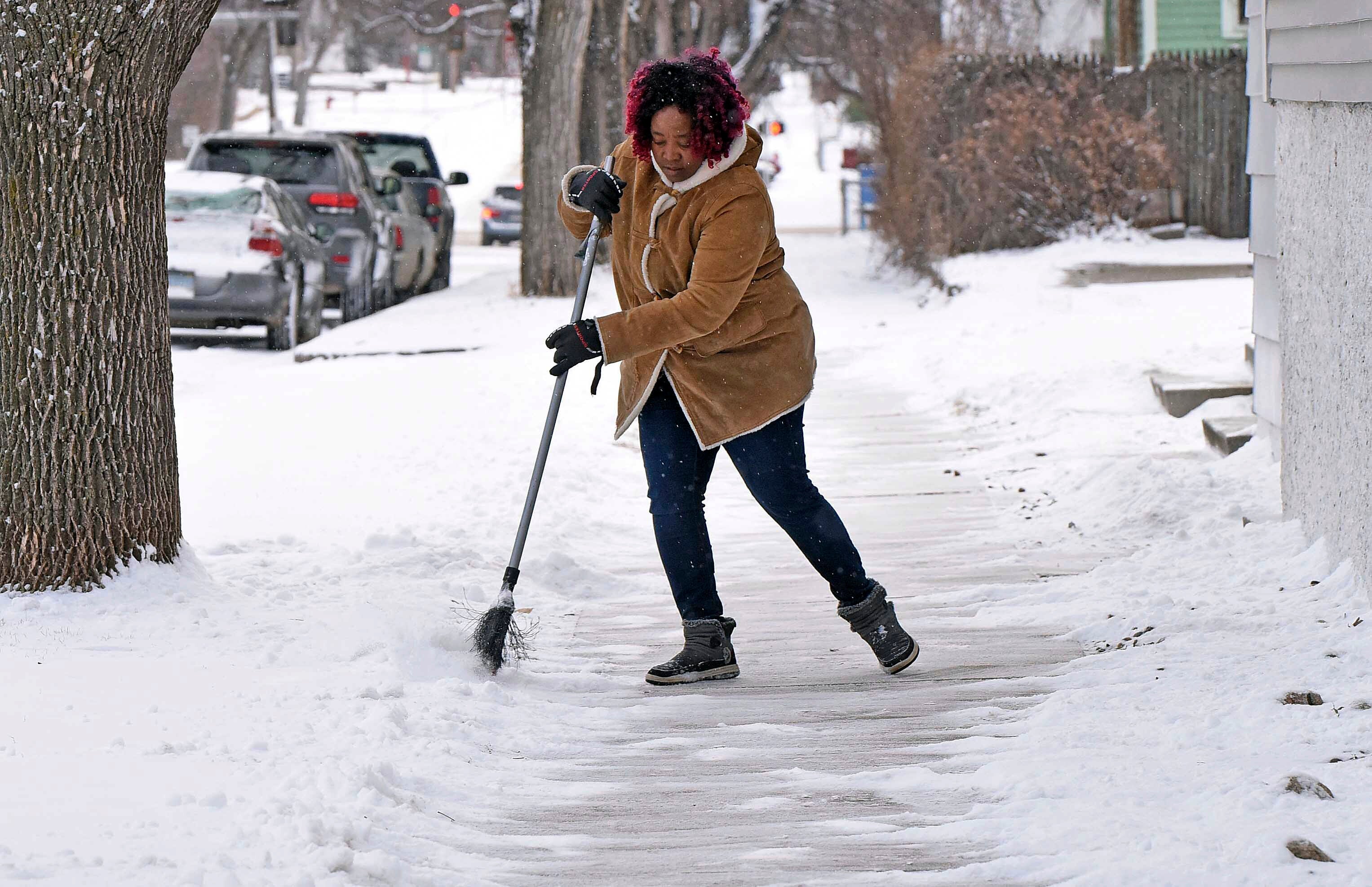 A woman sweeps the sidewalk of snow at the International Church Thursday, March 21, 2024 in Bismarck, N.D