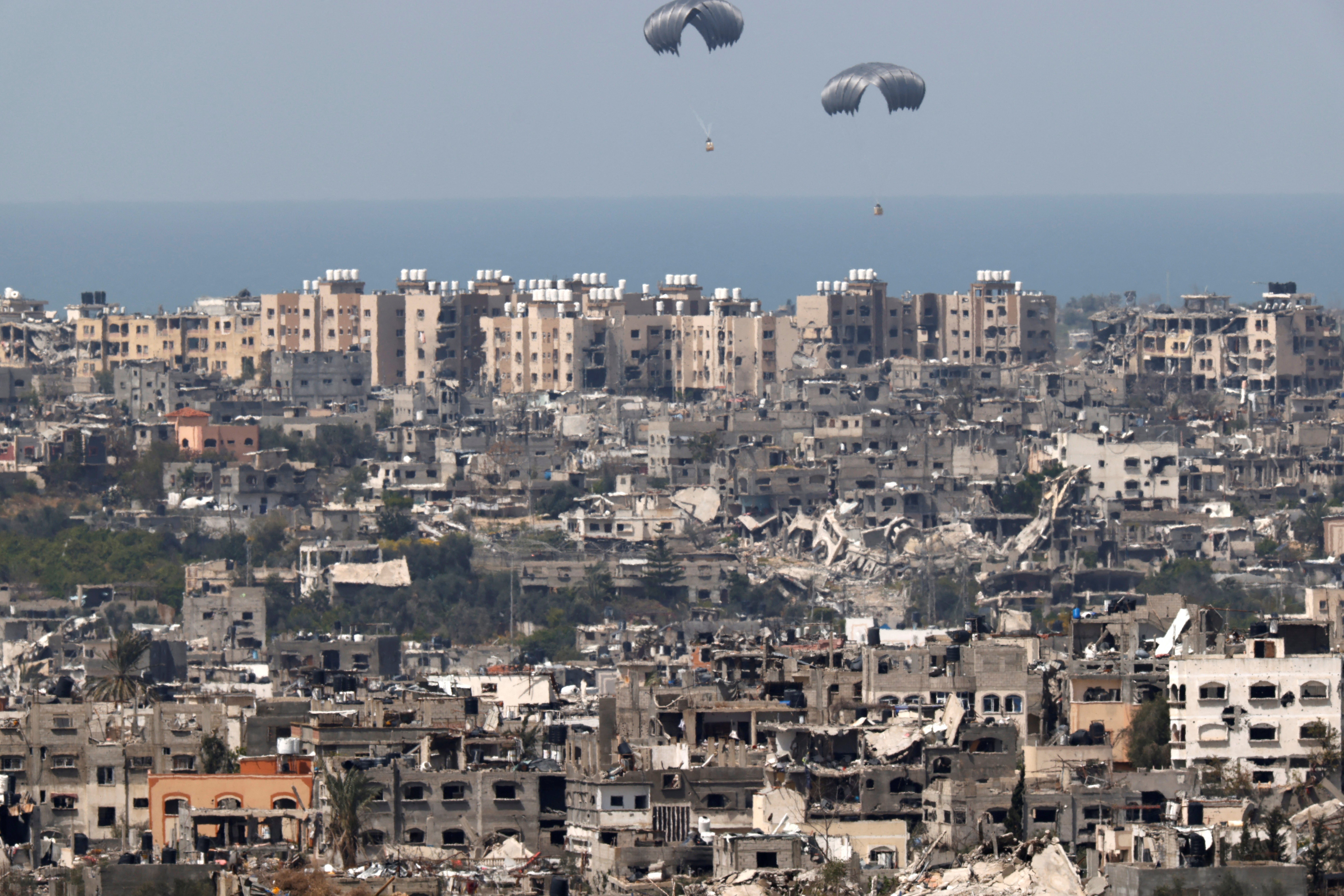 Humanitarian aid falls through the sky towards the Gaza Strip after being dropped from an aircraft