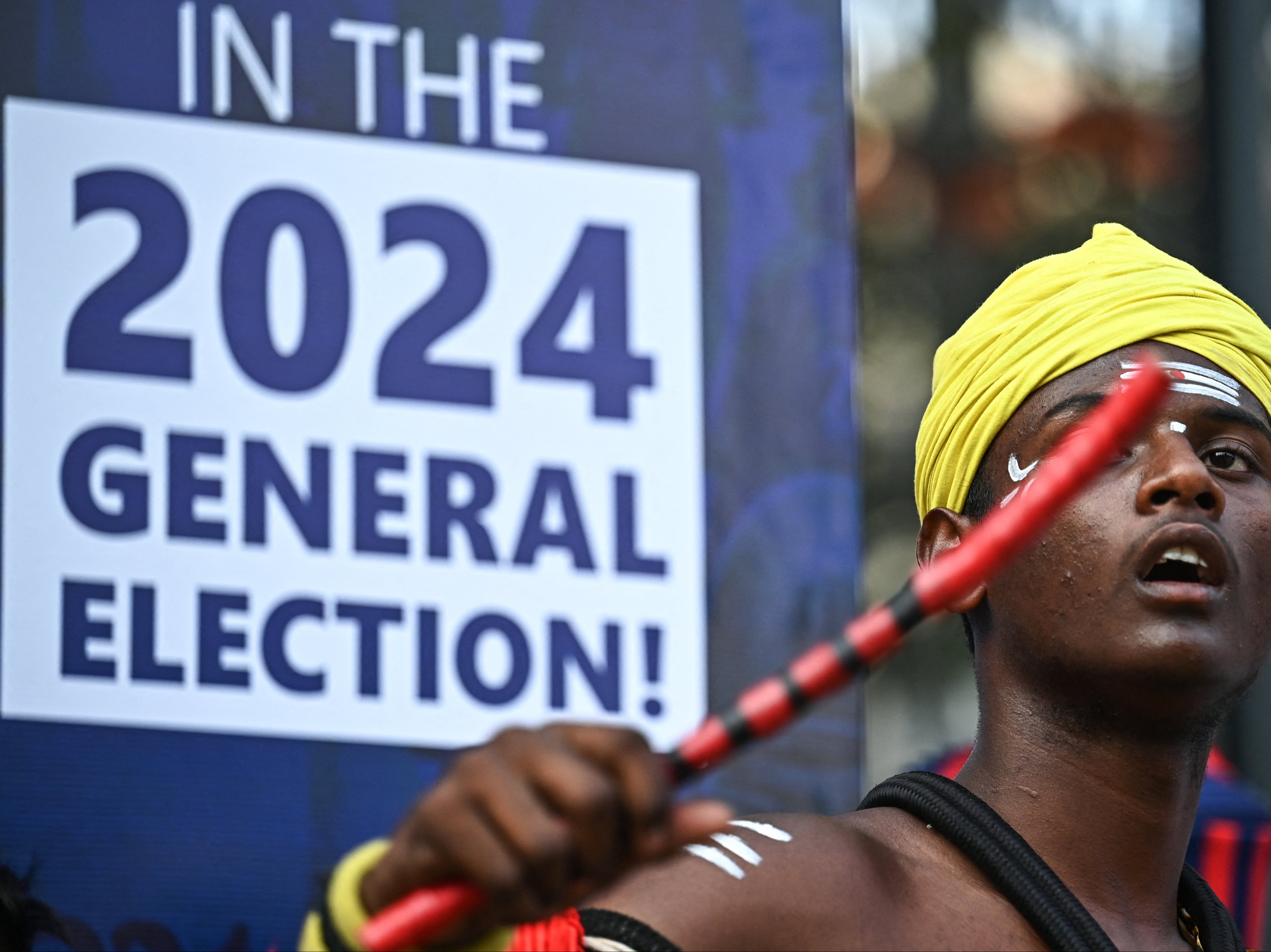 An artist dressed in traditional attire performs in front of an election sign board during the Vote-A-Thon, an awareness campaign organised by Karnataka’s Chief Electoral Office to encourage turnout for the upcoming 2024 general elections, in Bengaluru on 17 March 2024