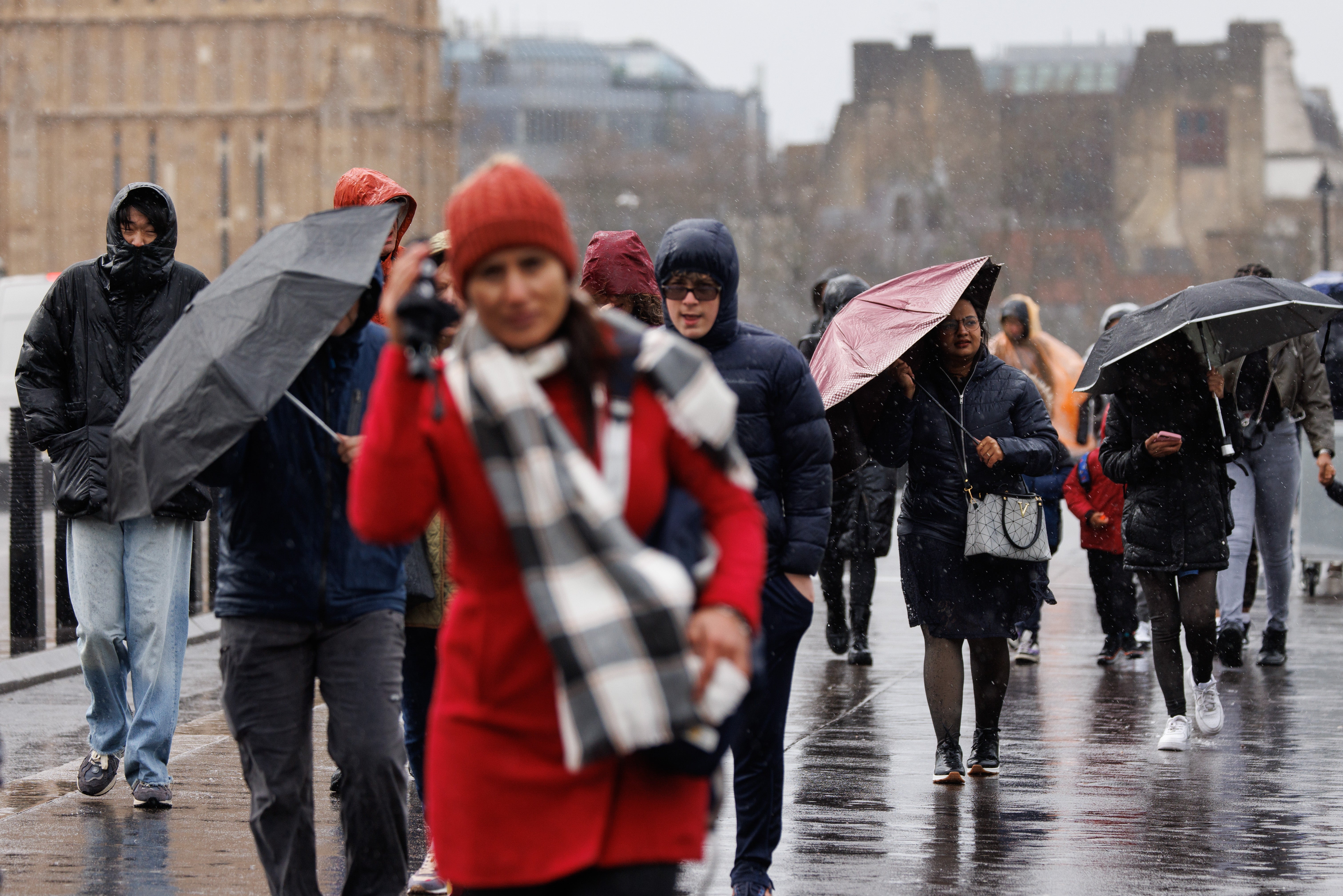 People walk across Westminster Bridge against strong winds and rain in London