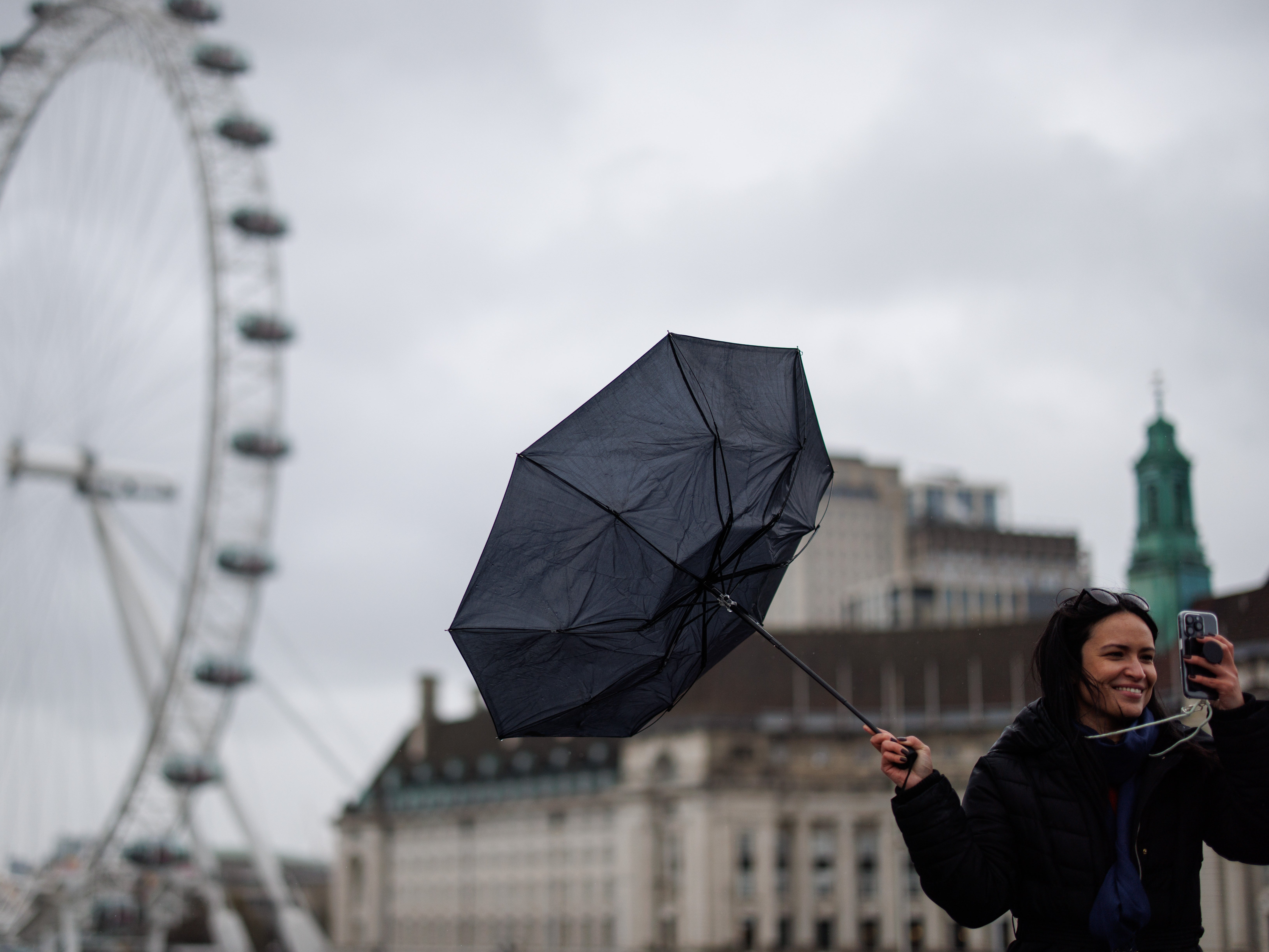 People walk across Westminster Bridge against strong winds in the rain with the London Eye in the background