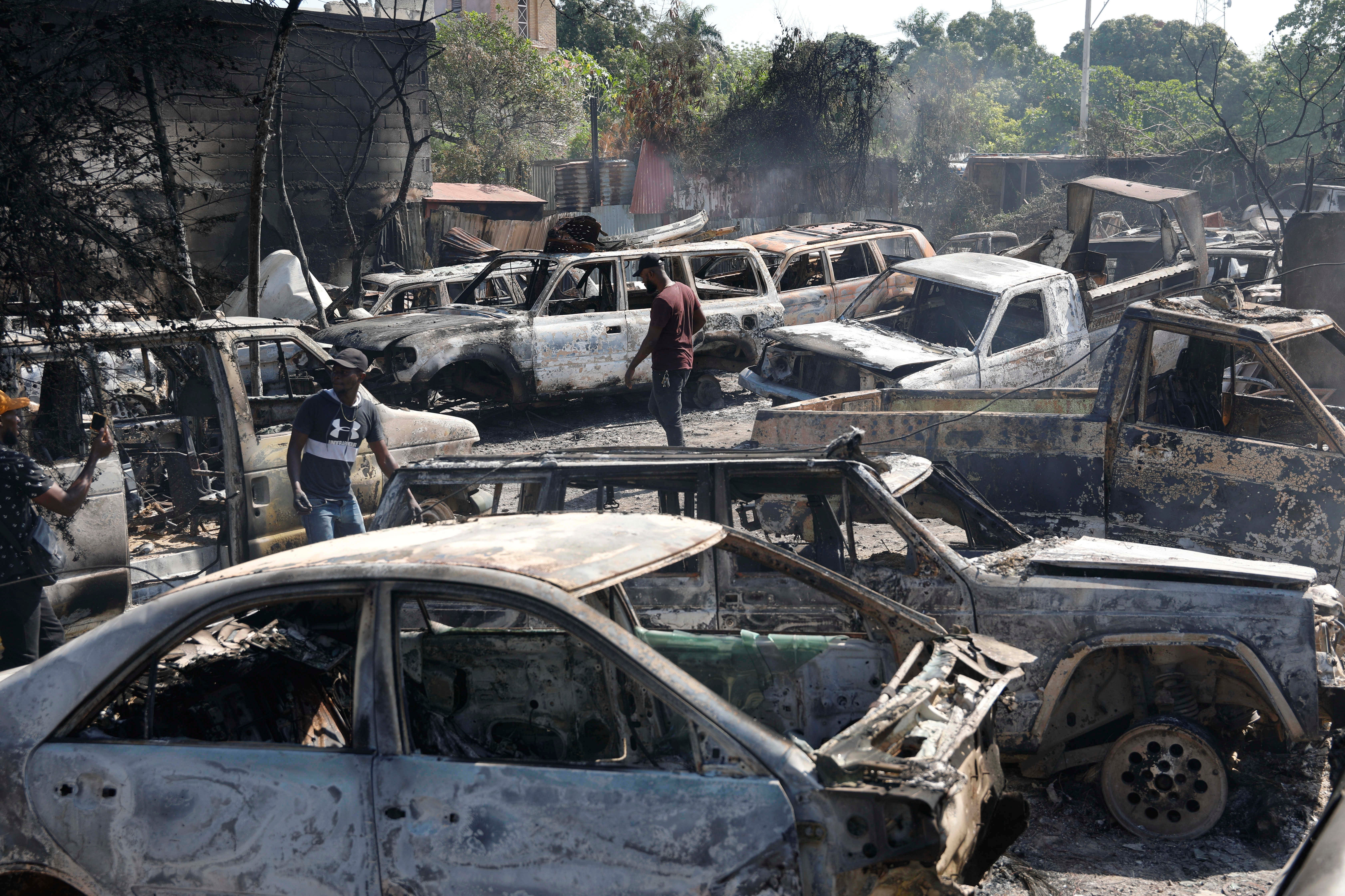 People look for salvageable parts among burnt-out cars at a mechanic shop that was set on fire during violence in Port-au-Prince
