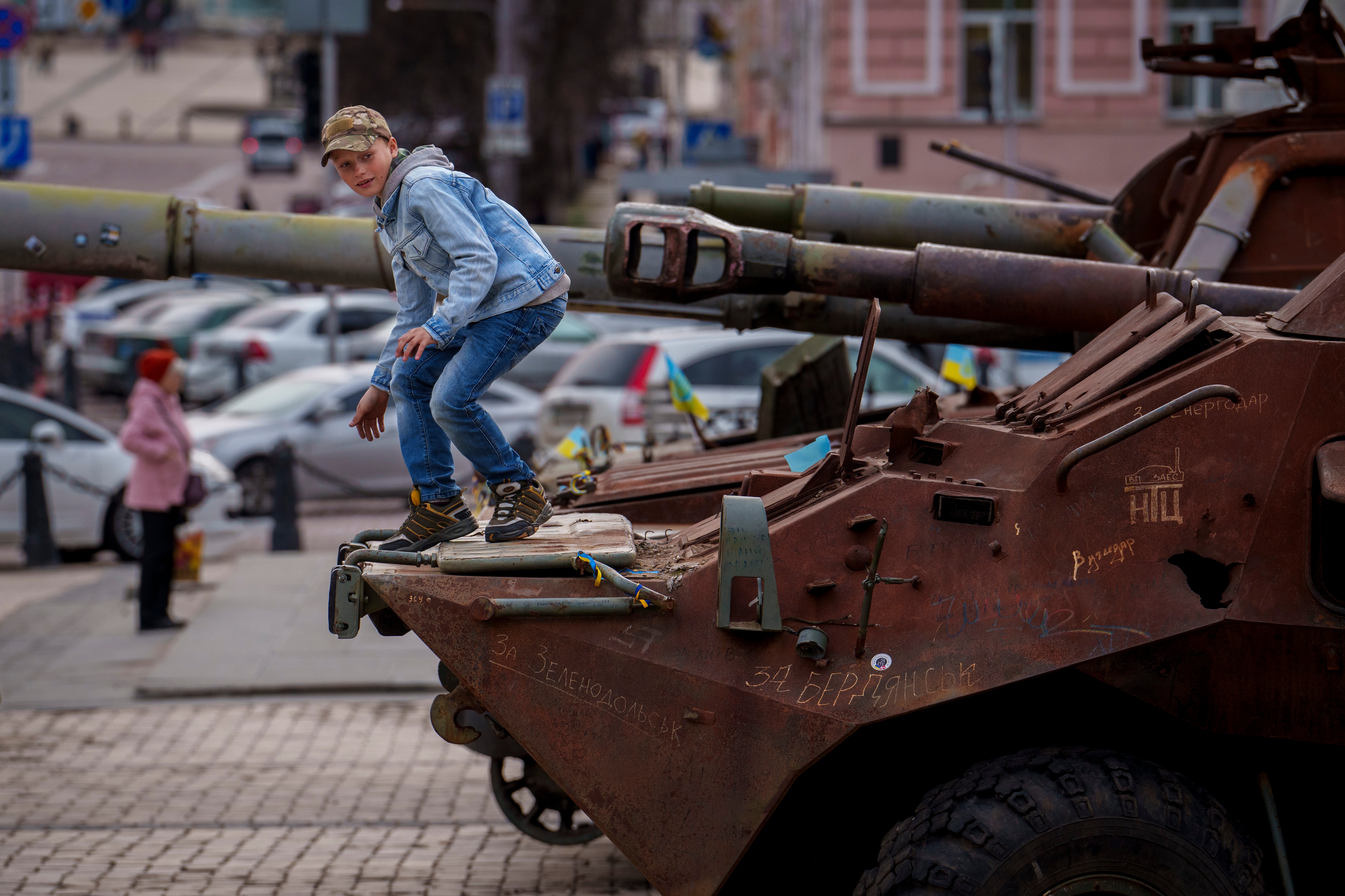 A child climbs on a rusty armored personnel carrier, part of a display of destroyed Russian military equipment in Kyiv