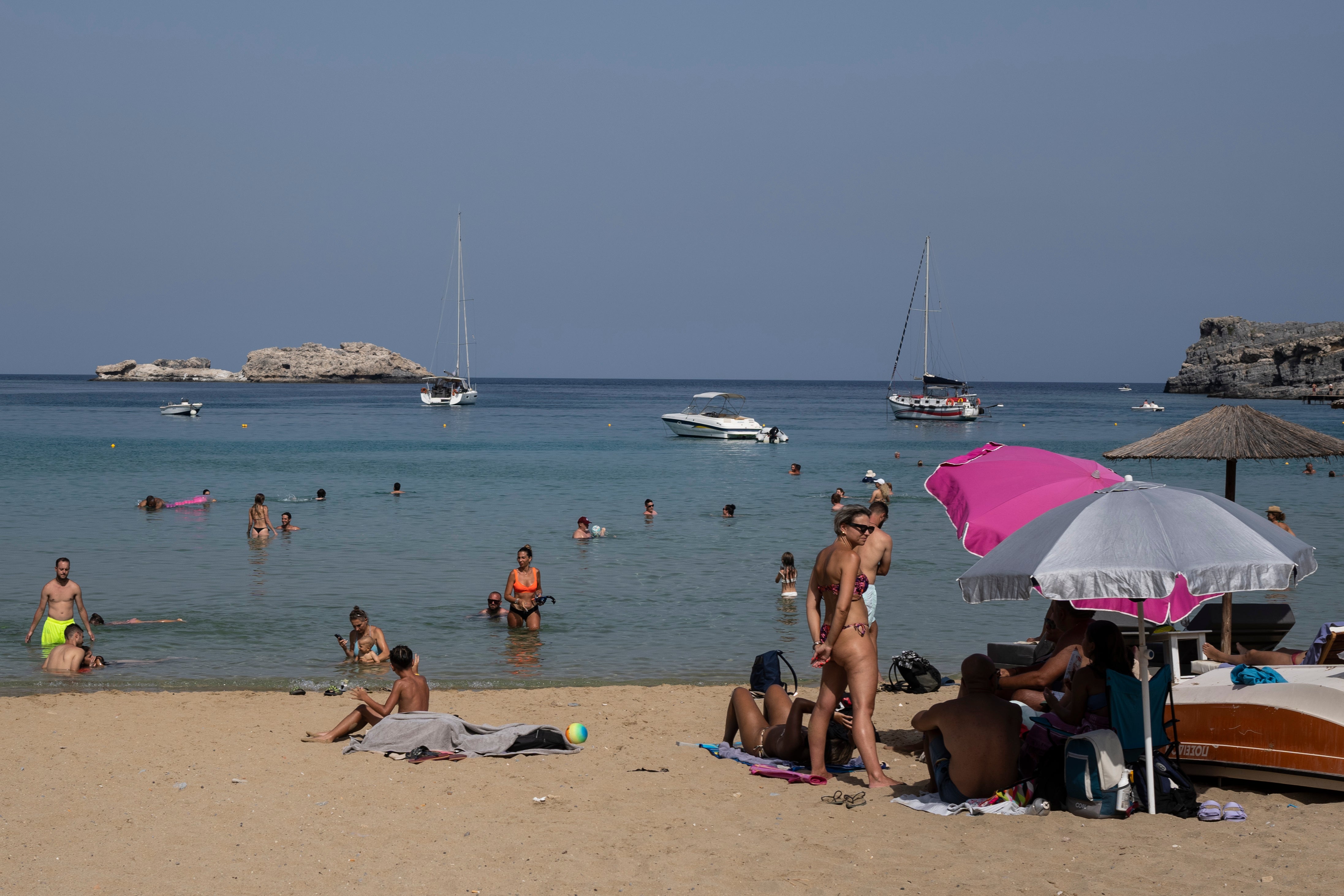 ourists enjoy the beach and the sea in Lindos, on the Aegean Sea island of Rhodes, southeastern Greece
