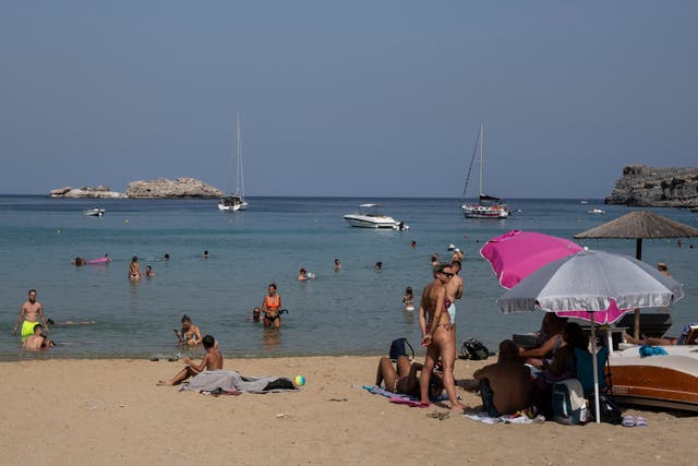 <p>ourists enjoy the beach and the sea in Lindos, on the Aegean Sea island of Rhodes, southeastern Greece</p>