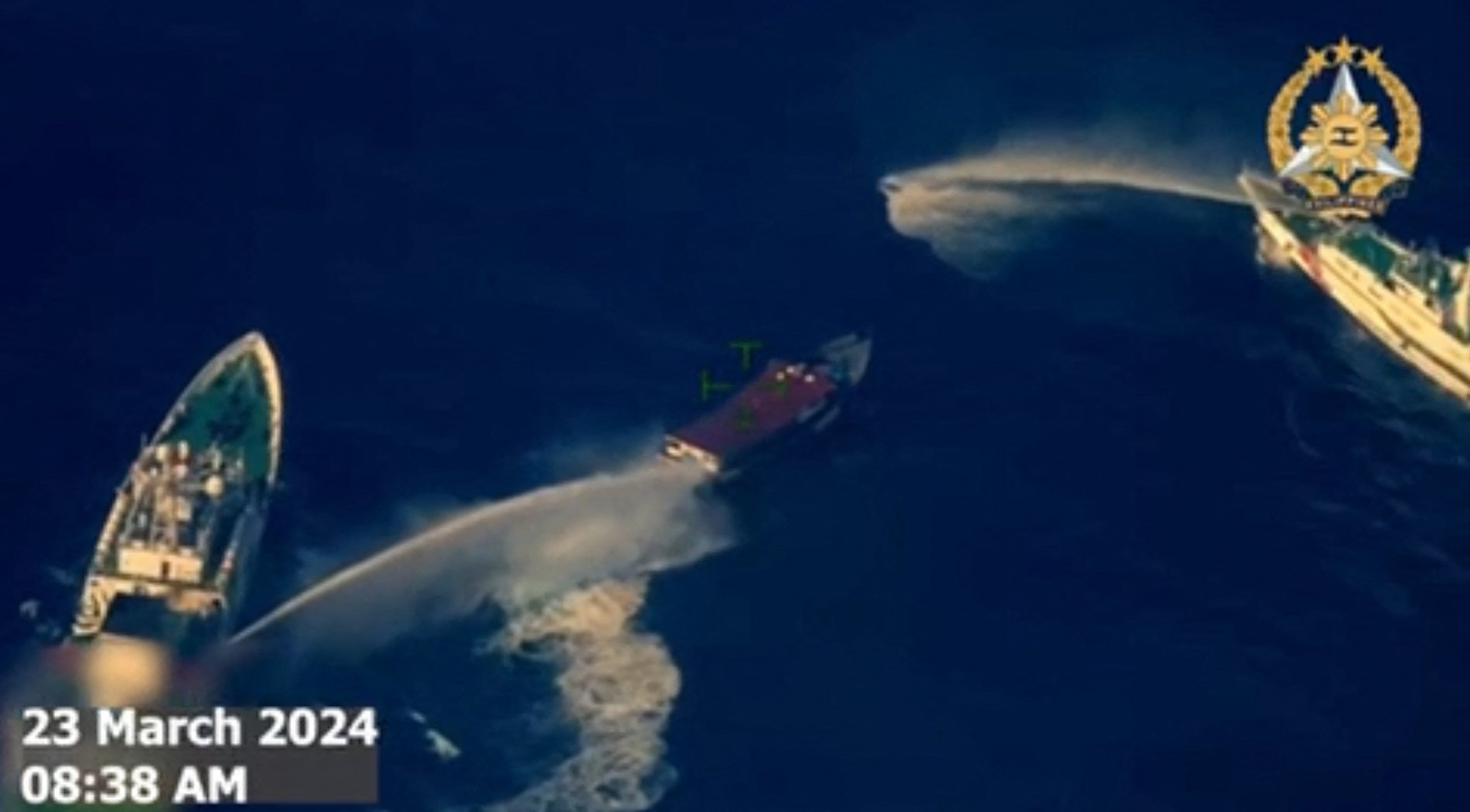 This frame grab from handout aerial video footage taken and released on 23 March 2024 by Philippines Armed Forces shows China Coast Guard ships (L and R) deploying water cannon against the Philippine military-chartered civilian boat Unaizah