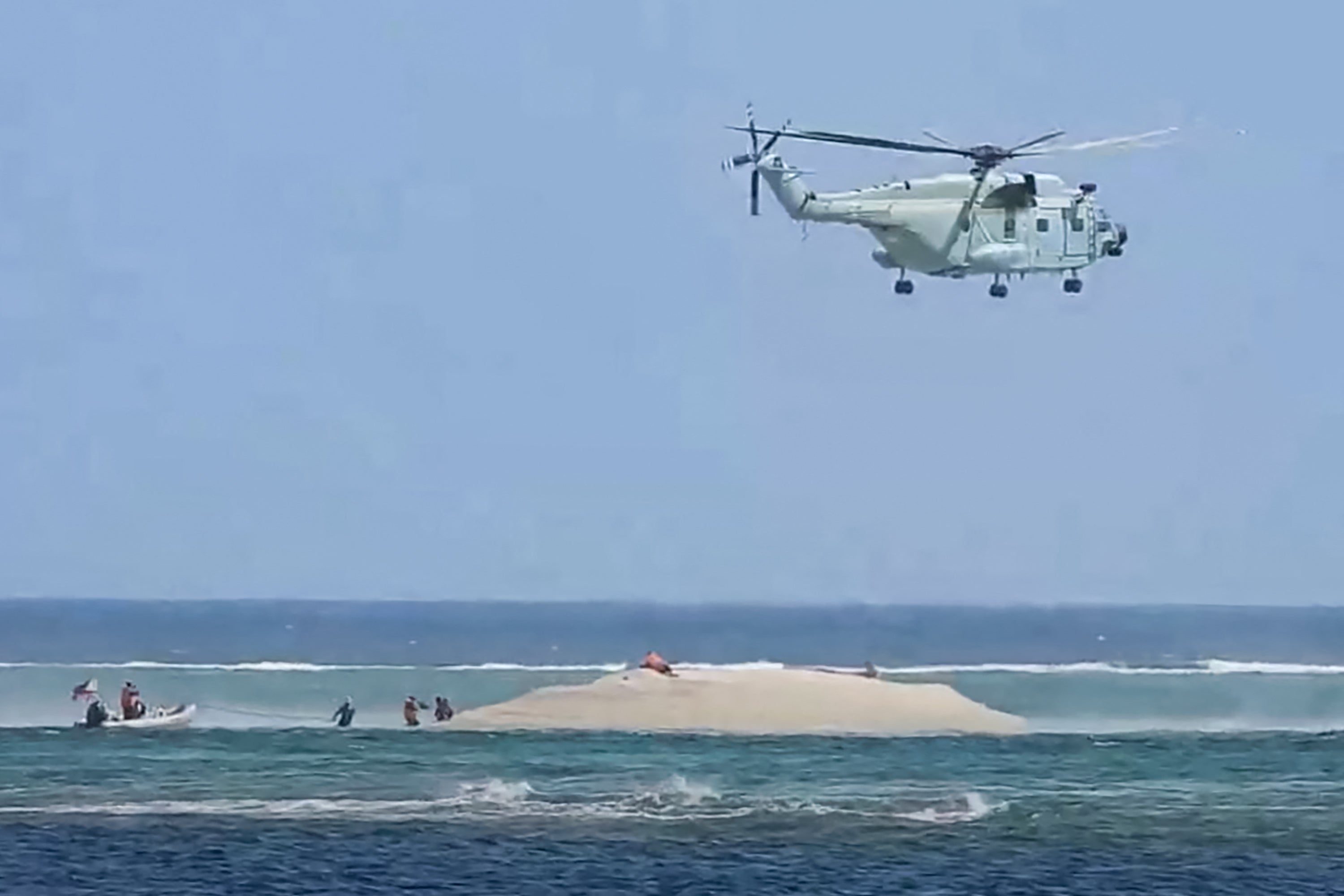 This frame grab from video footage taken and released on 25 March 2024 by the Philippine Bureau of Fisheries and Aquatic Resources (PCG/BFAR) shows a Chinese helicopter hovering as Philippine scientists inspect a cay near the Philippine-held Thitu Island, in the Spratly Islands, in the disputed South China Sea