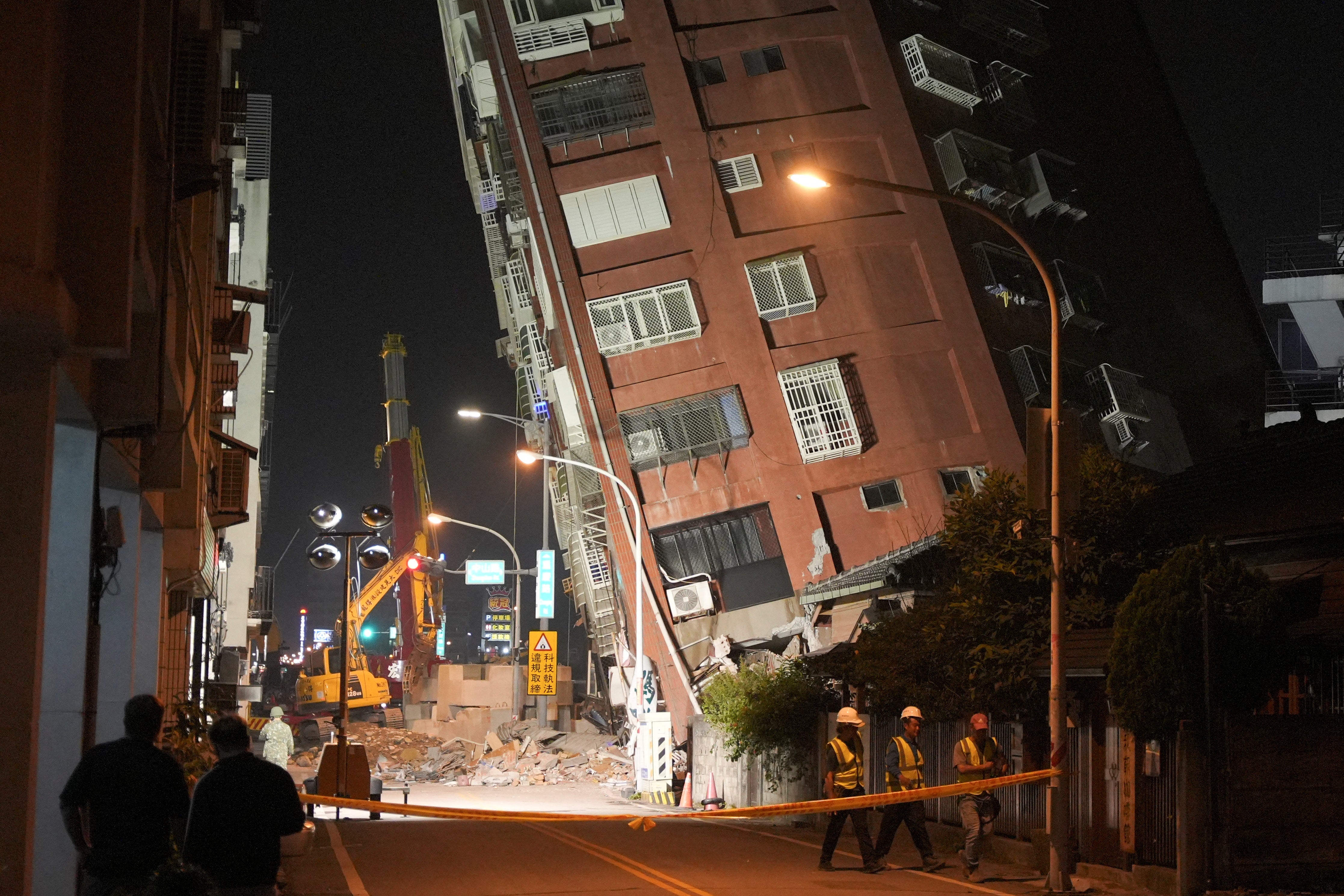 <p>Workers walk at the site where a building collapsed, following an earthquake, in Hualien, Taiwan</p>