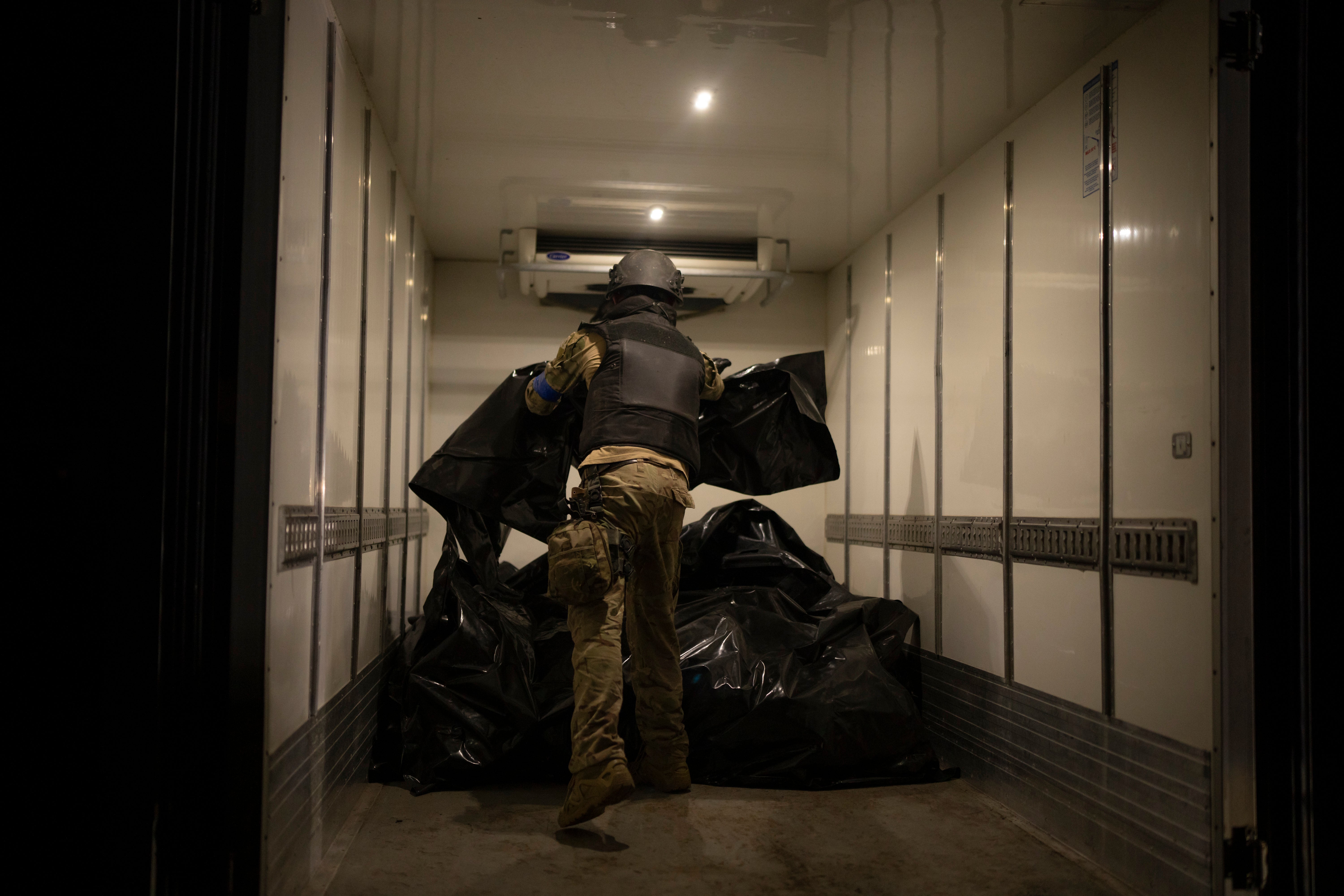 A member of Oleksii Yukov’s body collector team piles the bodies of deceased Russians in a refrigerated truck