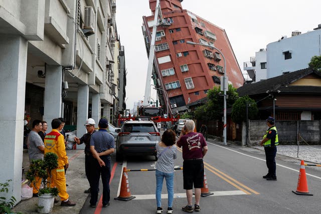 <p>People look on as work is carried out on a partially-collapsed building following the earthquake </p>