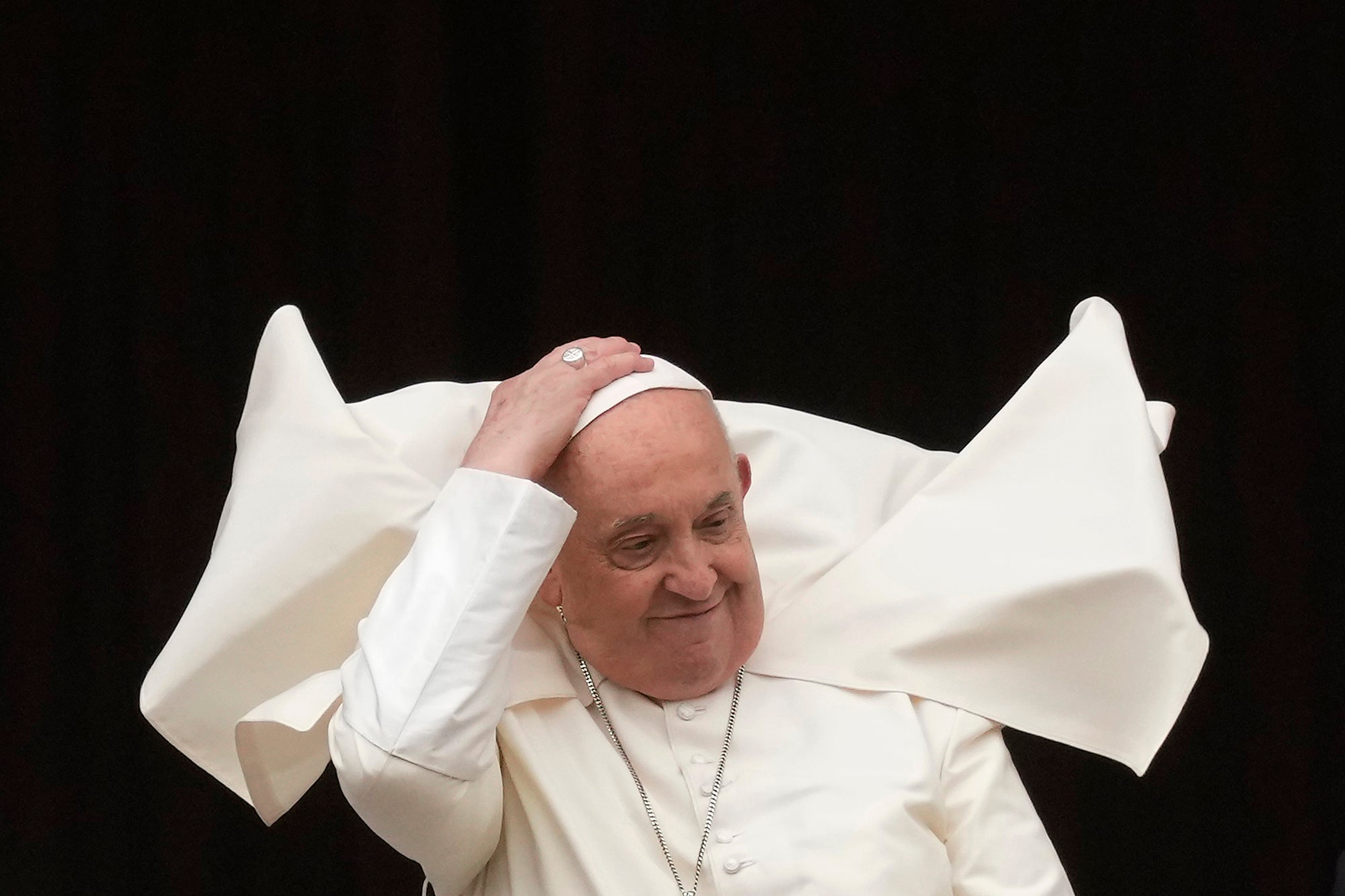 Pope Francis holds his skull cap to prevent it blowing in the wind