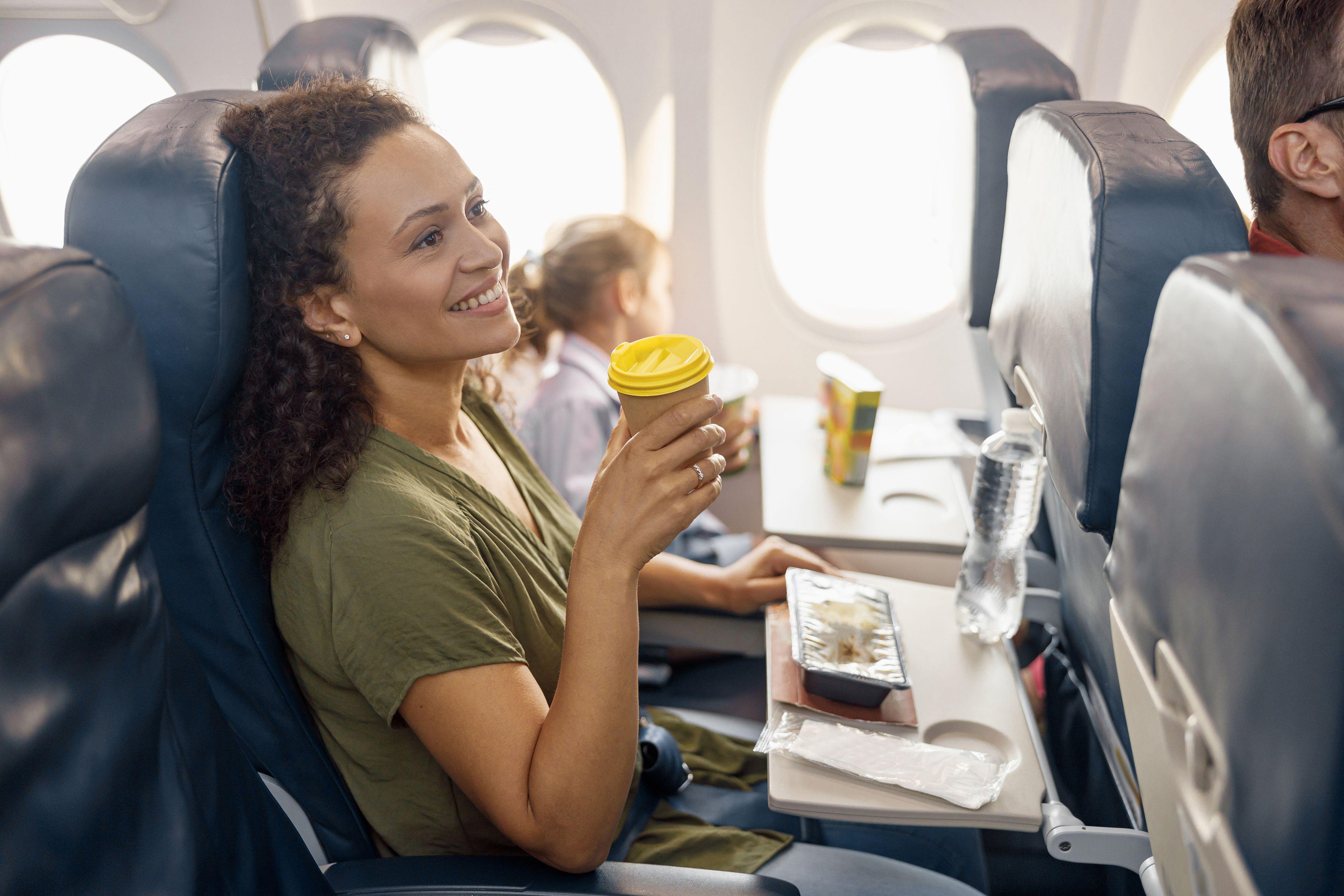 A lady drinking a hot beverage on a flight