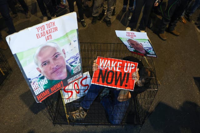 <p>A man sits in a cage with portraits of 47-year-old Israeli hostage Elad Katzir as relatives and supporters of Israeli hostages held in Gaza since the October 7 attacks by Hamas militants, stage a demonstration in Tel Aviv, on March 26, 2024</p>
