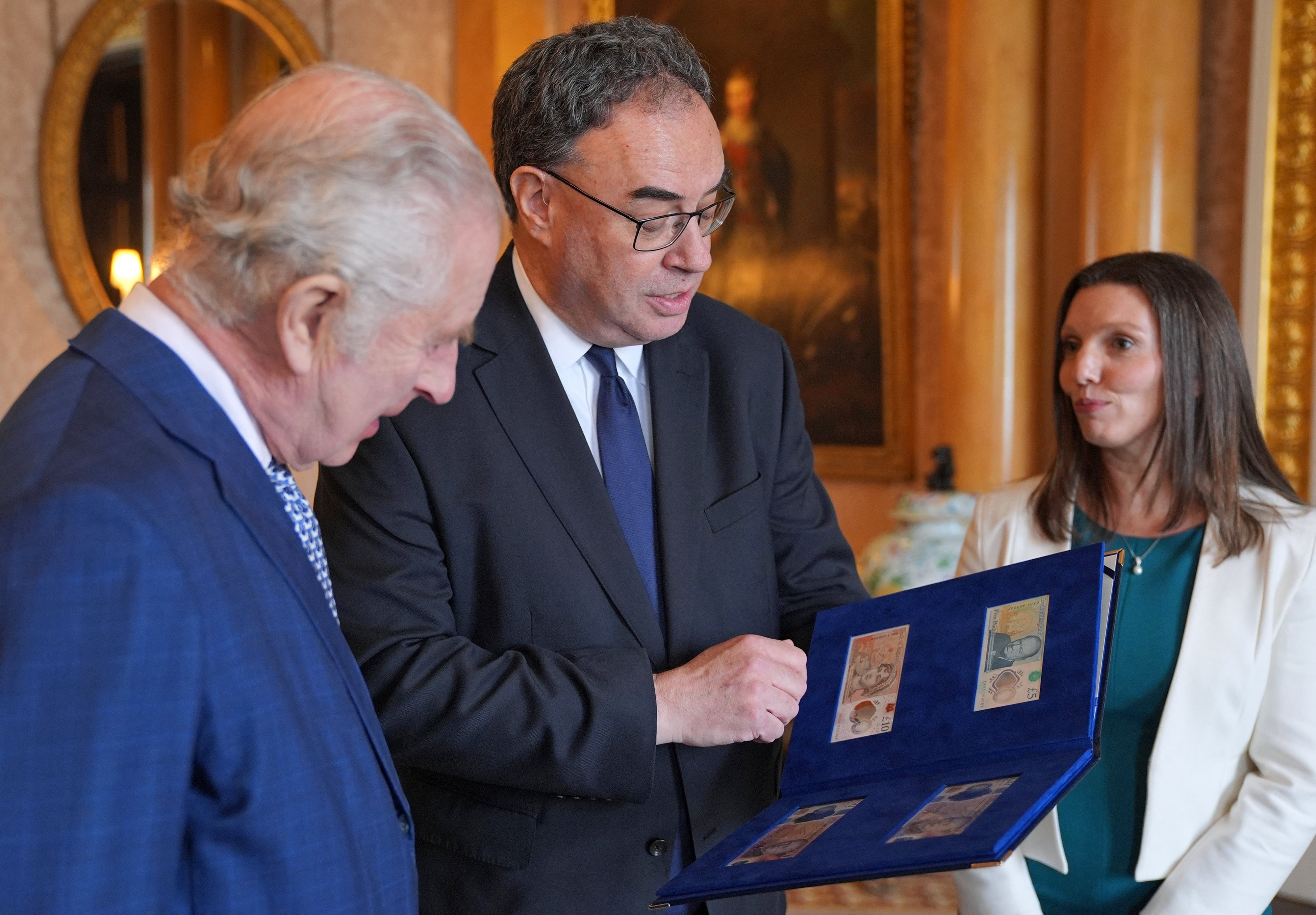 King Charles III (L) is reacts as Bank of England Governor Andrew Bailey (C) and Bank of England's Chief Cashier Sarah John present him with the first bank notes featuring his portrait, at Buckingham Palace in London on April 9, 2024
