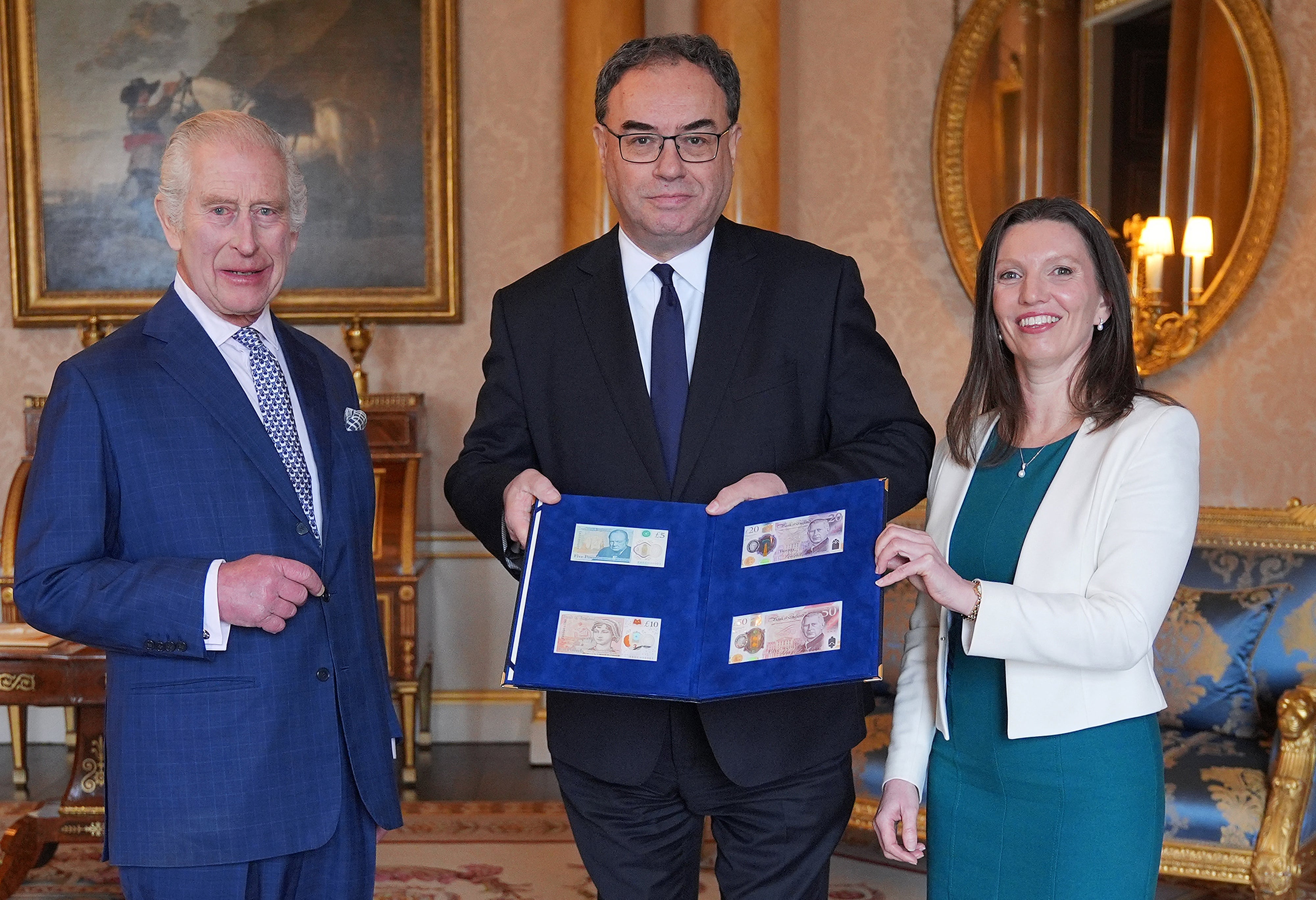 Britain's King Charles III (L) is reacts as Bank of England Governor Andrew Bailey (C) and Bank of England's Chief Cashier Sarah John present him with the first bank notes featuring his portrait