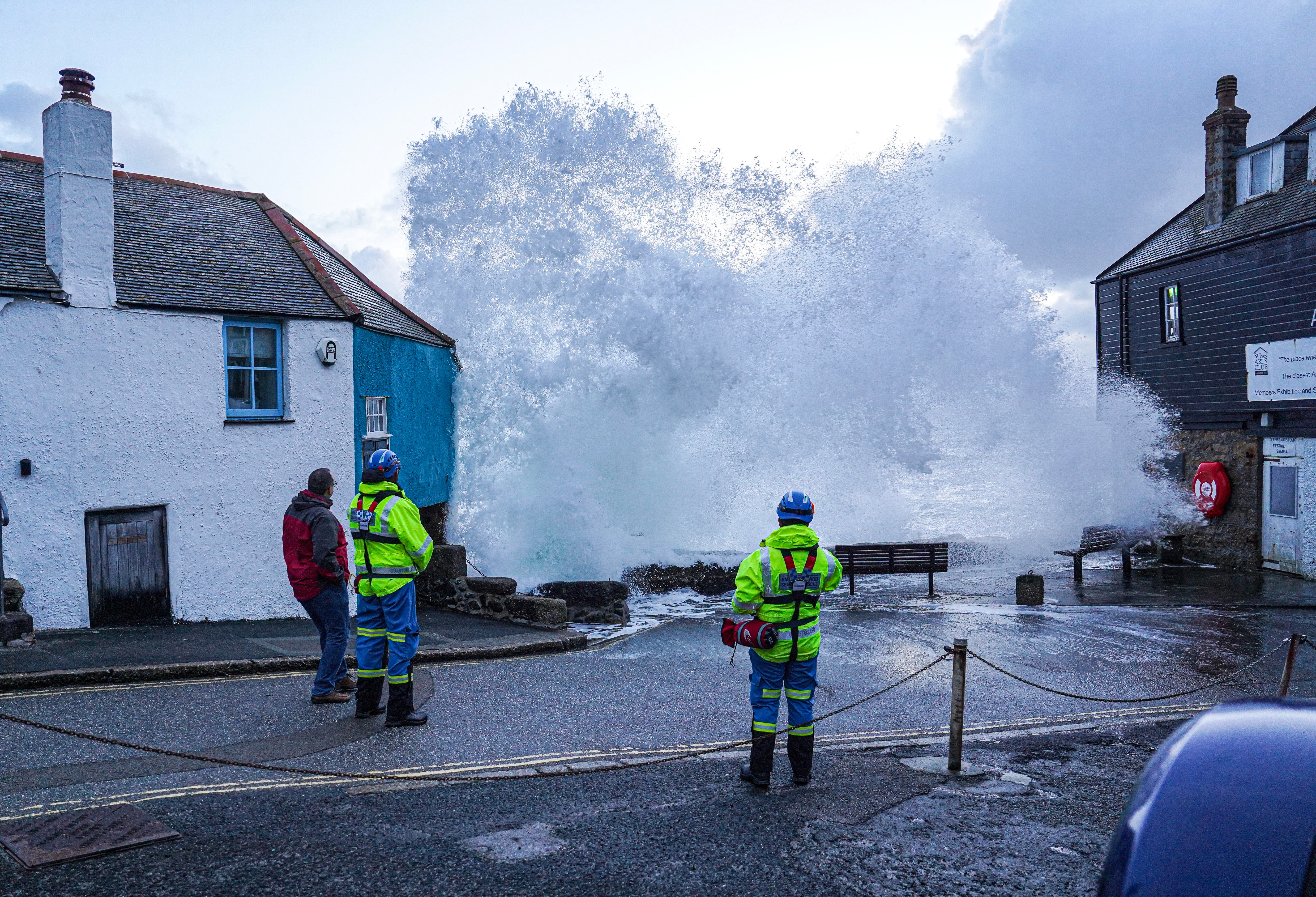 HM Coastguard personnel look on as waves crash over the harbour wall onto the street in St Ives