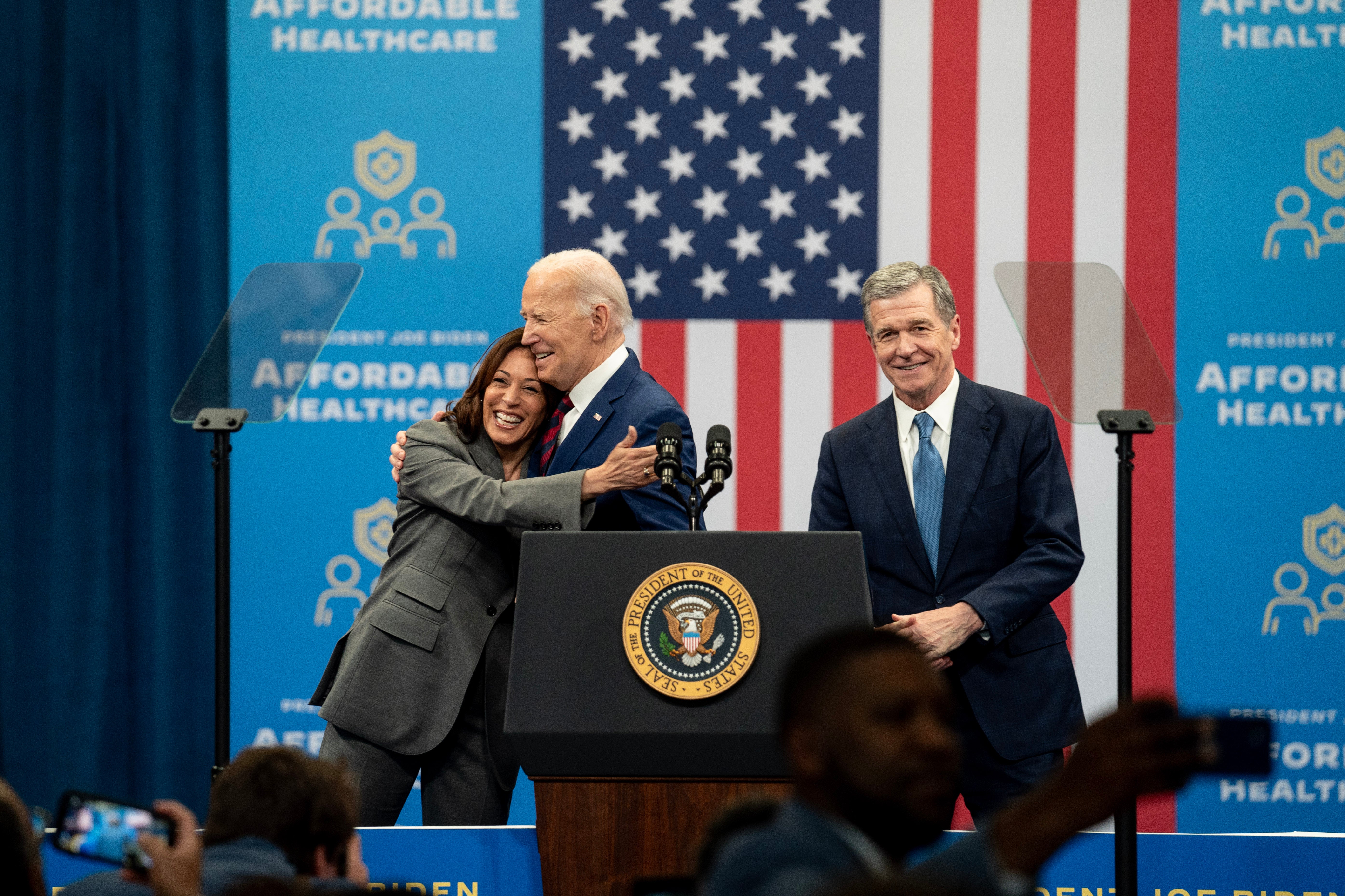 US President Joe Biden hugs Kamala Harris, the vice-president, as Roy Cooper, the governor of North Carolina, looks on during an event at the Chavis community centre on 26 March 2024 in Raleigh, North Carolina