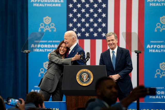 <p>US President Joe Biden hugs Kamala Harris, the vice-president, as Roy Cooper, the governor of North Carolina, looks on during an event at the Chavis community centre on 26 March 2024 in Raleigh, North Carolina</p>