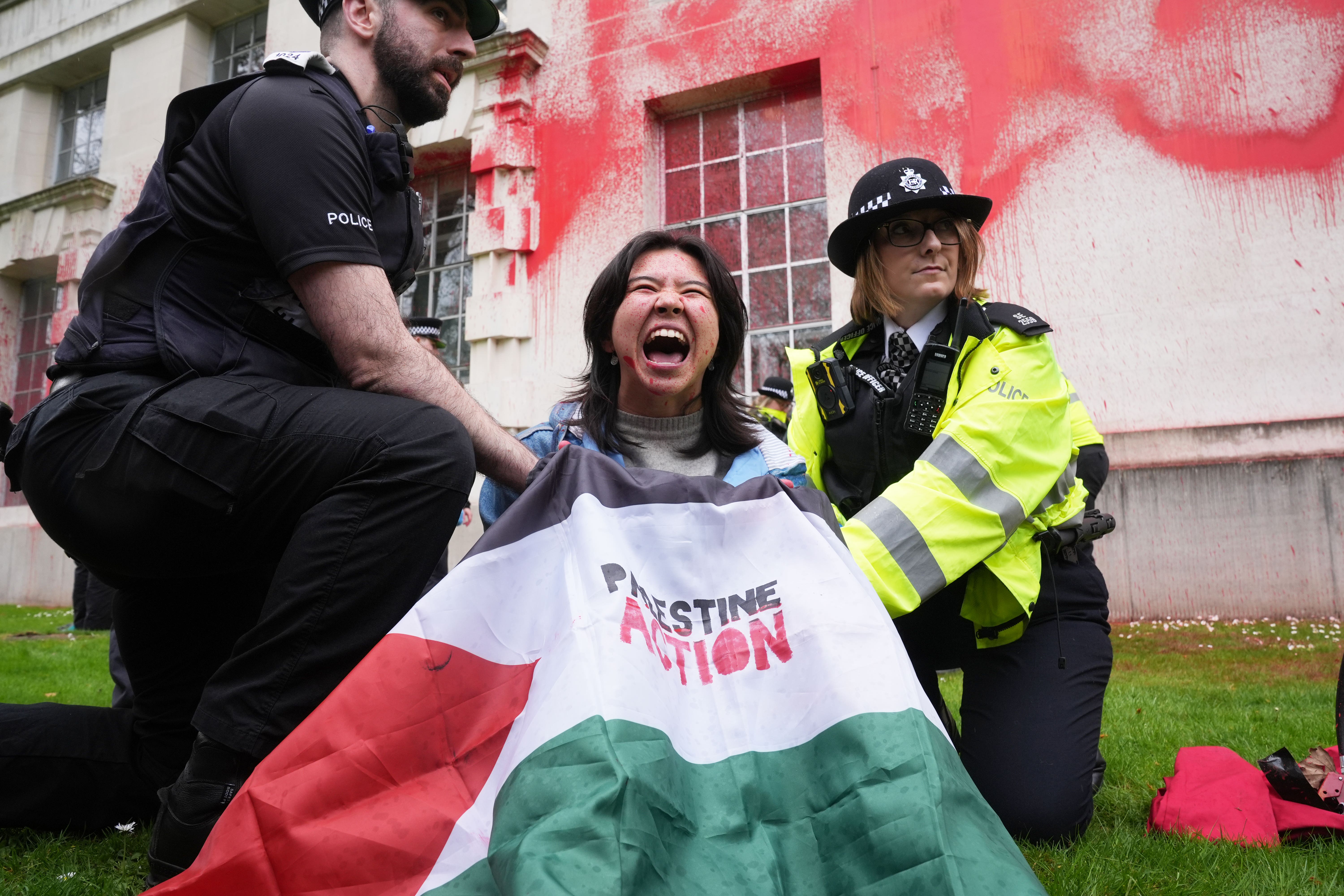 Police officers detain a person after members of Youth Demand threw red paint over the outside of the Ministry of Defence building in London (Lucy North/PA)