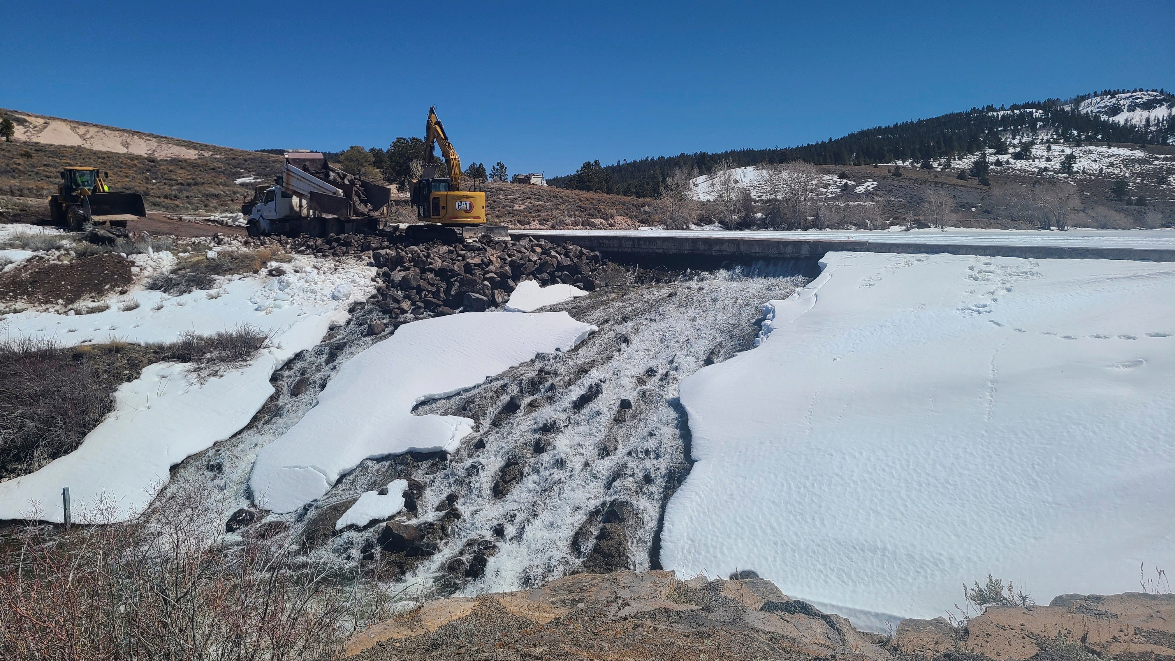 Crews use heavy machinery to place boulders downstream of the cracked Panguitch Lake Dam to reinforce the wall, Wednesday, April 10, 2024, in Panguitch, Utah